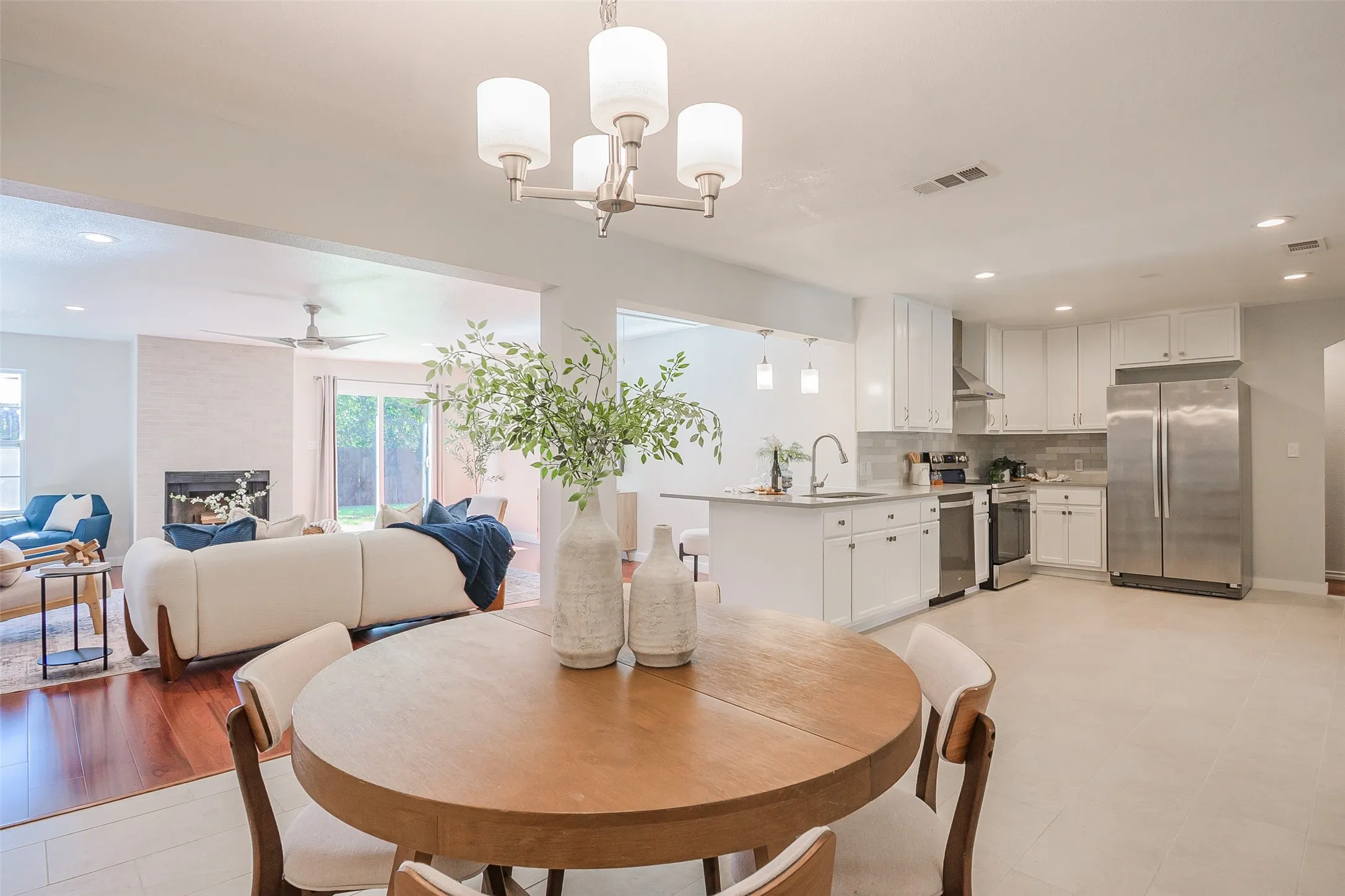 Open-concept area featuring white cabinetry, stainless steel appliances, kitchen island, recessed lighting, and a fireplace with a light-toned surround