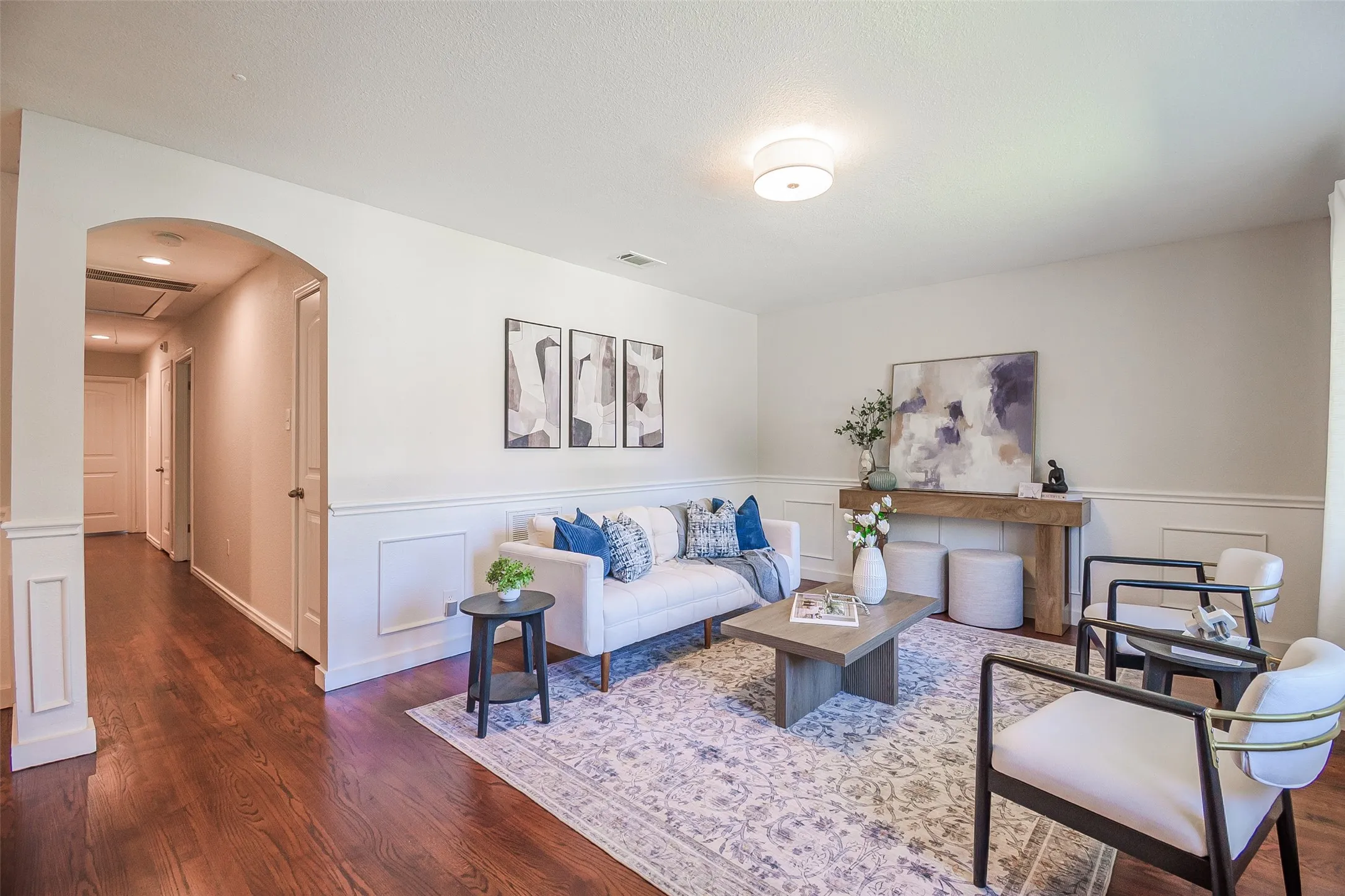 Wood-finish flooring, architectural archway with column detailing, and wainscoting throughout