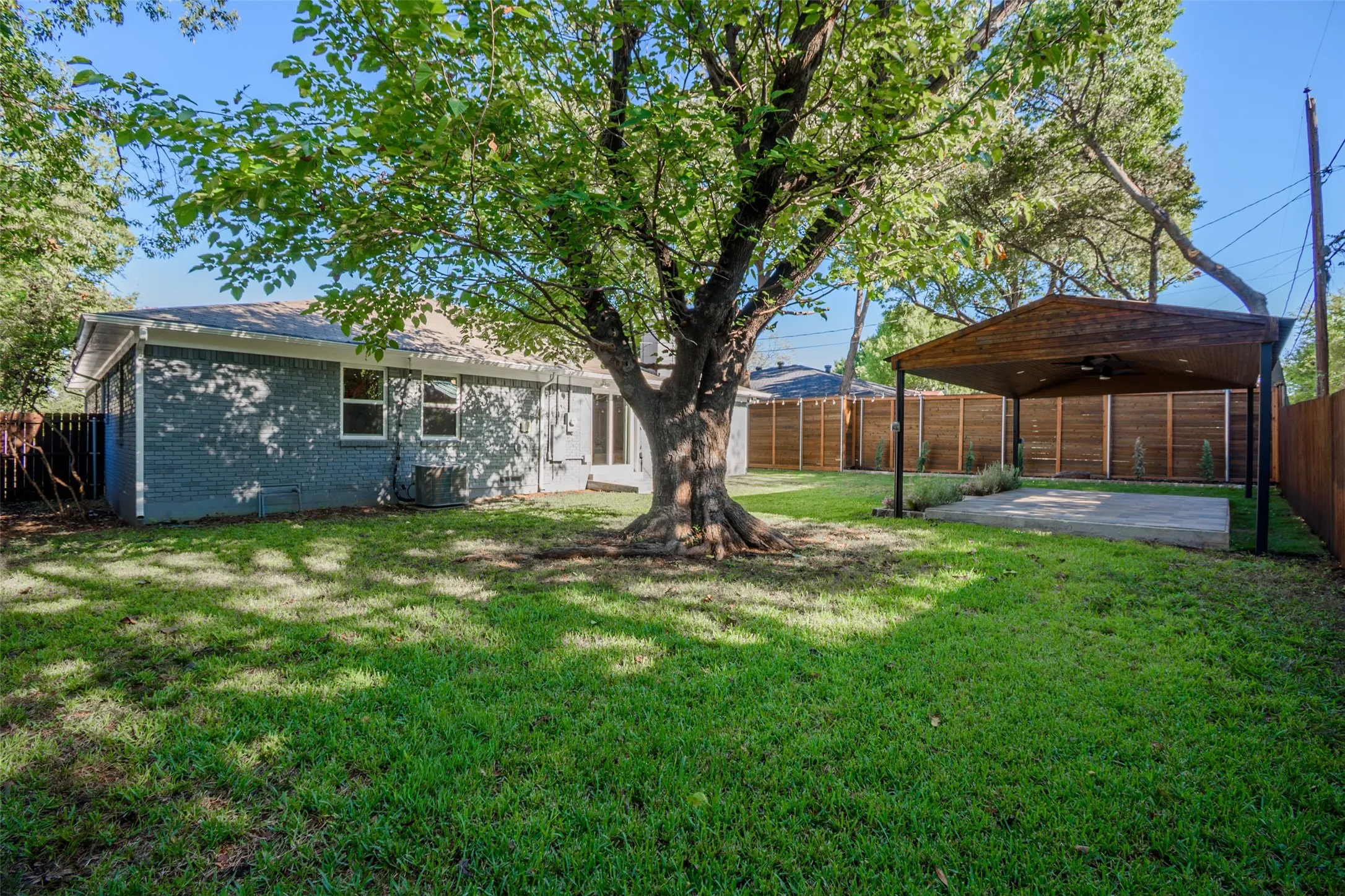 Backyard featuring a painted brick exterior, large mature tree, covered patio, and full wood perimeter fencing