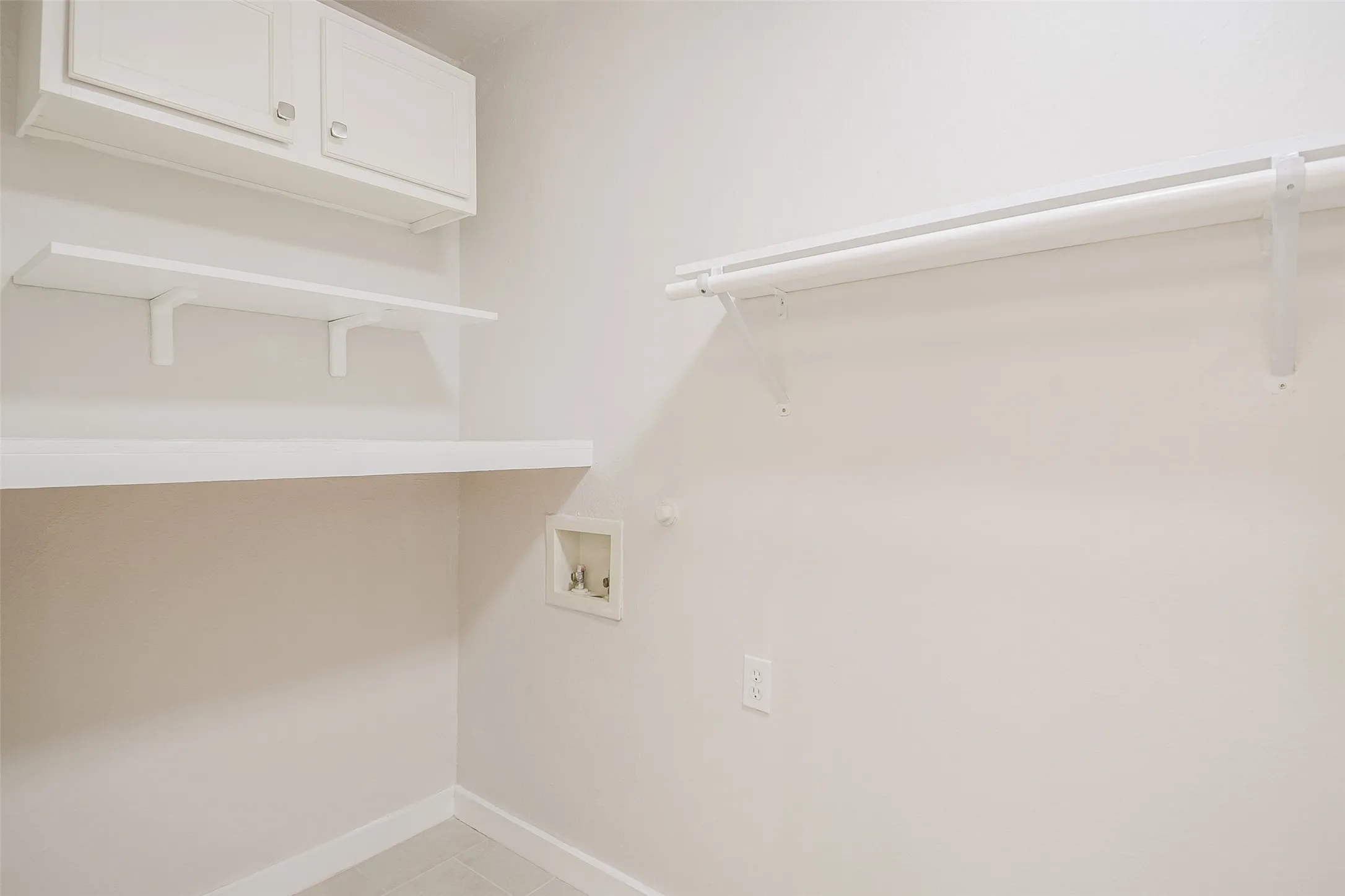 Wall-mounted white cabinetry, open shelving, and a metal clothing rod with integrated support brackets