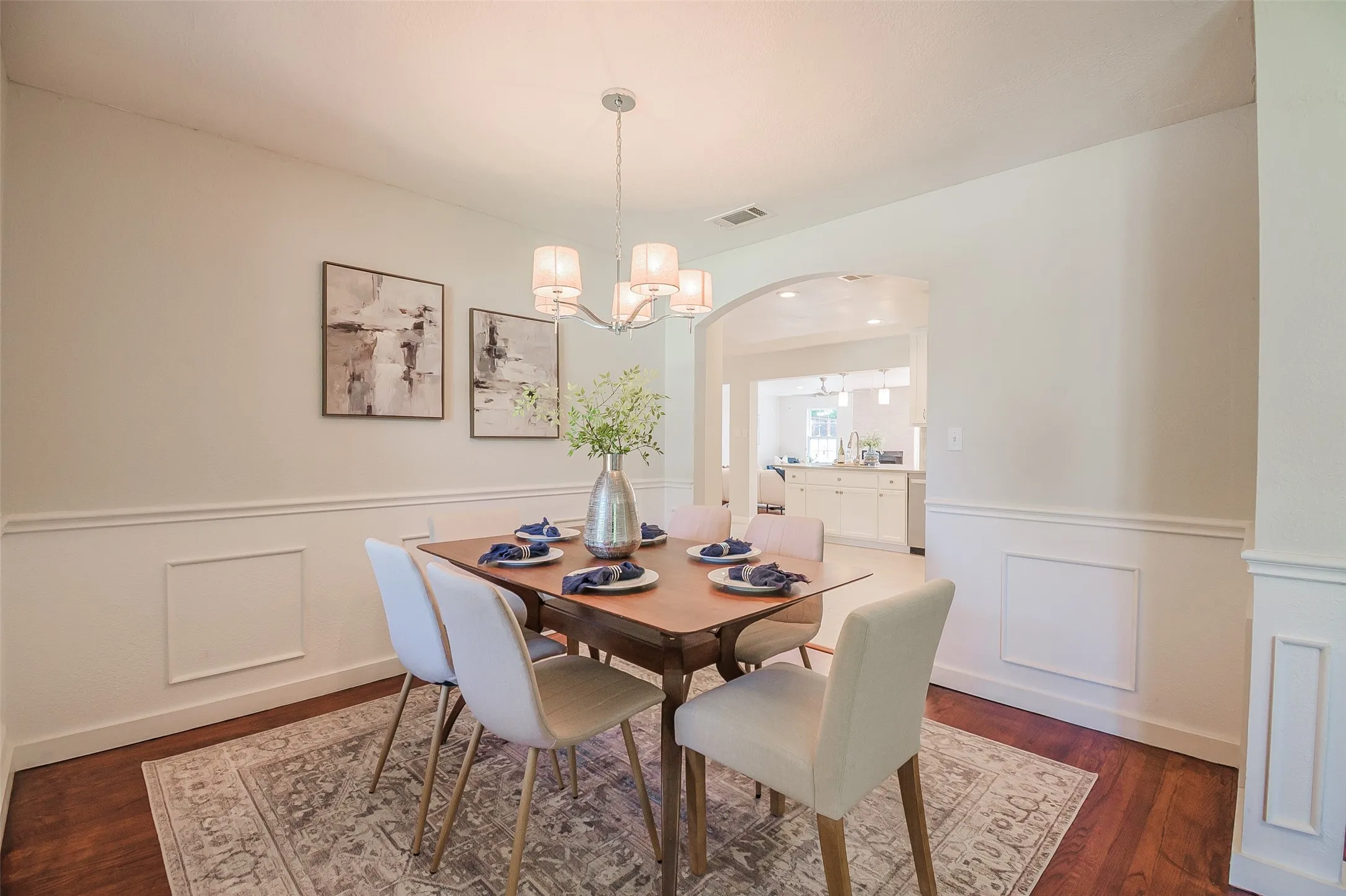 Dining area featuring wood-finish flooring, wainscoting, and a multi-light chandelier under a high ceiling
