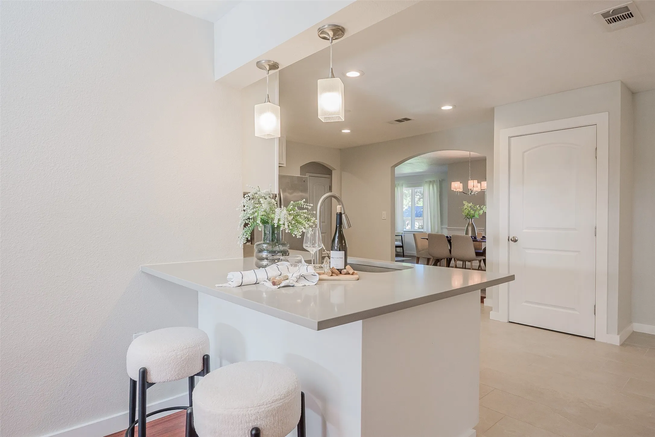 Kitchen island with solid surface countertop and undermount sink, illuminated by dual hanging pendant lights and featuring an arched architectural opening