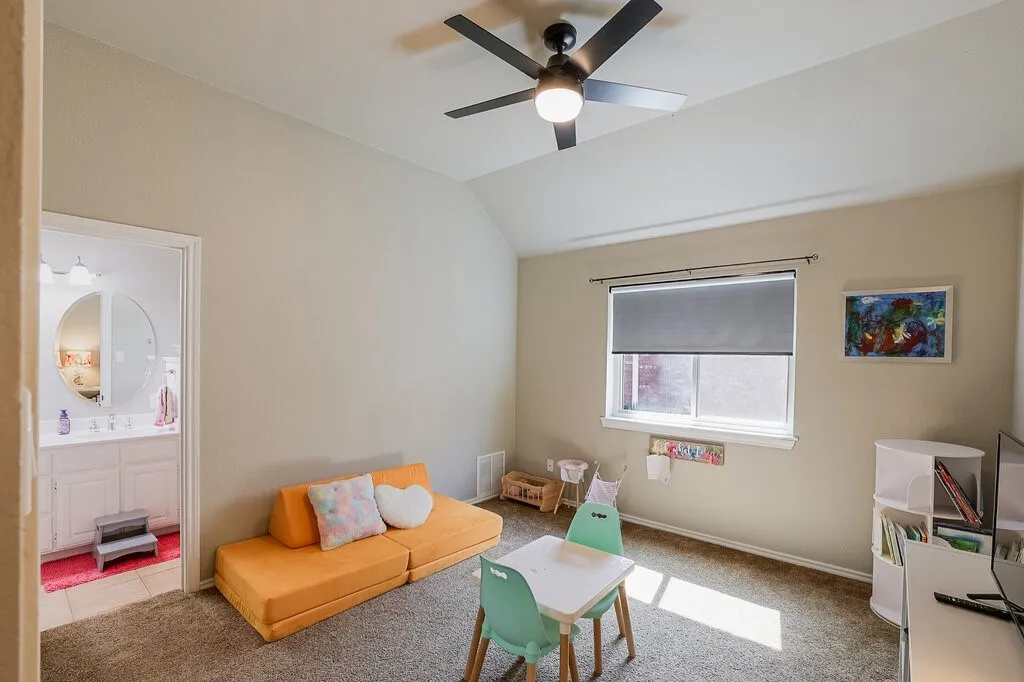 Vaulted ceiling with a matte black ceiling fan, neutral carpeting, and a roller shade window treatment
