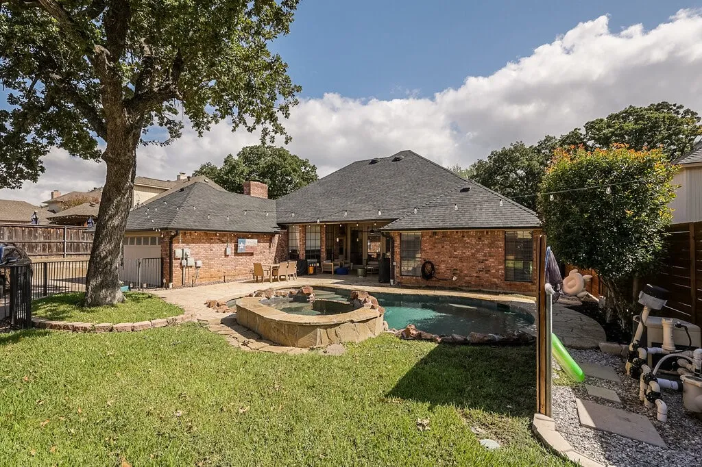 Brick exterior residence featuring an in-ground pool with stone coping, raised stone spa, paver patio, and mature trees