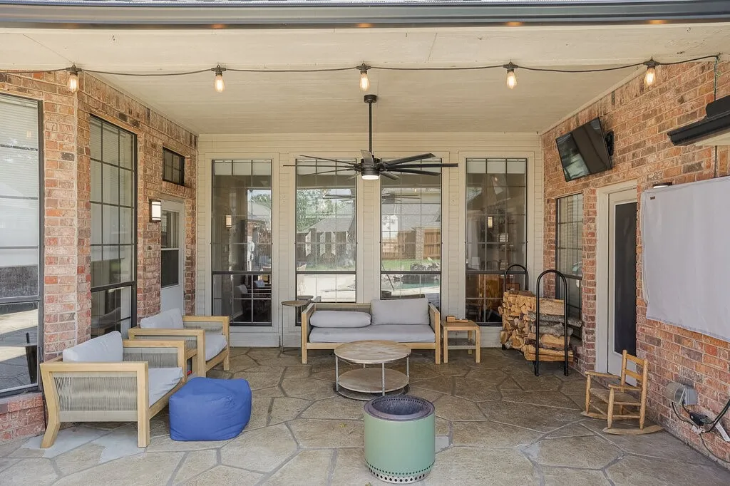 Covered patio featuring flagstone flooring, red brick walls, overhead ceiling fan, and integrated string lighting