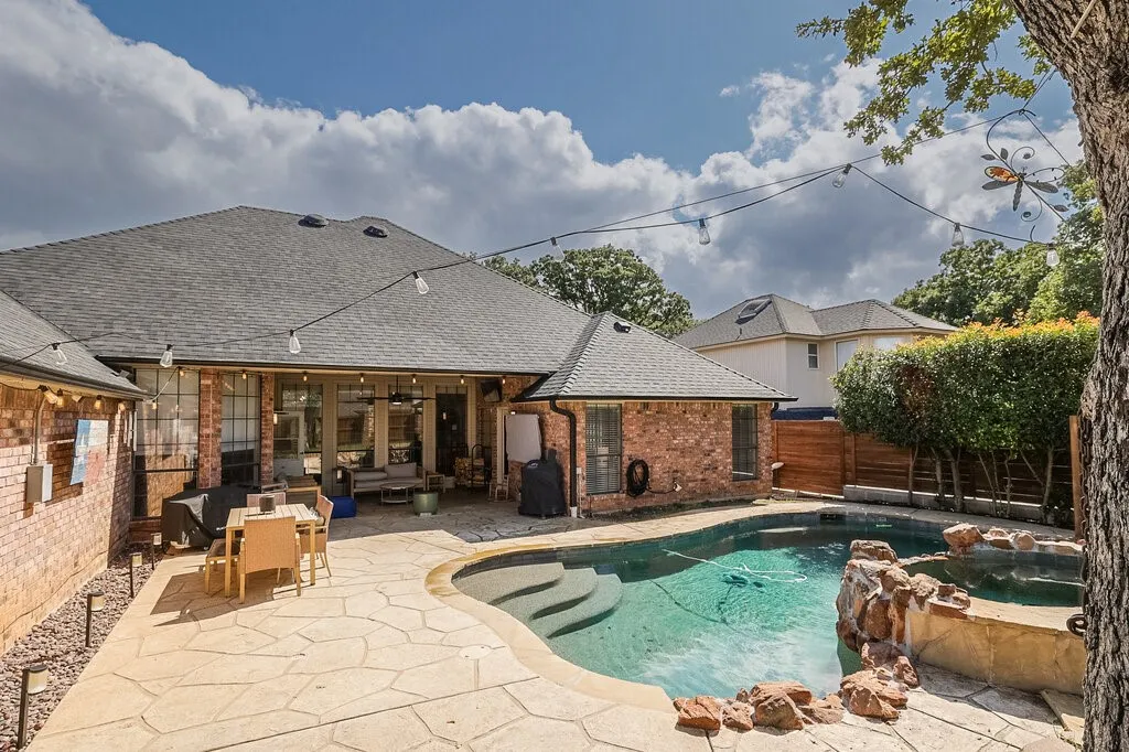 Backyard featuring a brick exterior, flagstone patio, custom-shaped swimming pool, and stone-accented spa