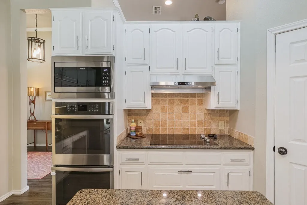 Kitchen featuring white cabinetry with silver-tone hardware, stone countertops, a tiled backsplash, a built-in stainless steel double wall oven, and a built-in microwave
