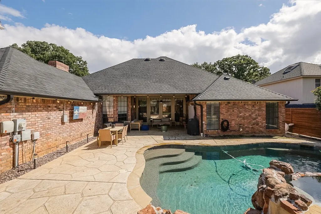 Brick exterior, covered patio, flagstone-patterned concrete decking, and in-ground pool with stone water feature