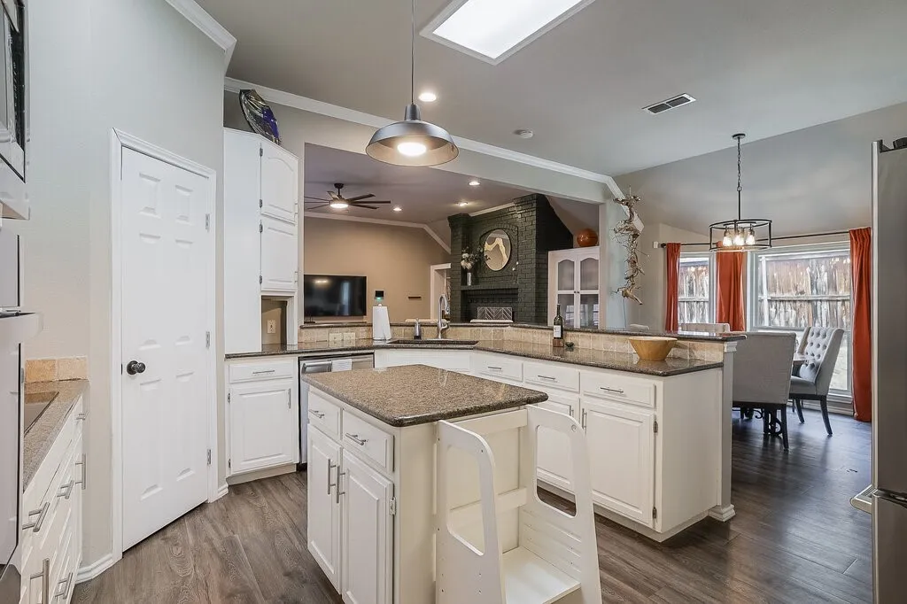 Kitchen featuring a center island, white cabinetry, stone countertops, pendant lighting, and wood-finish flooring