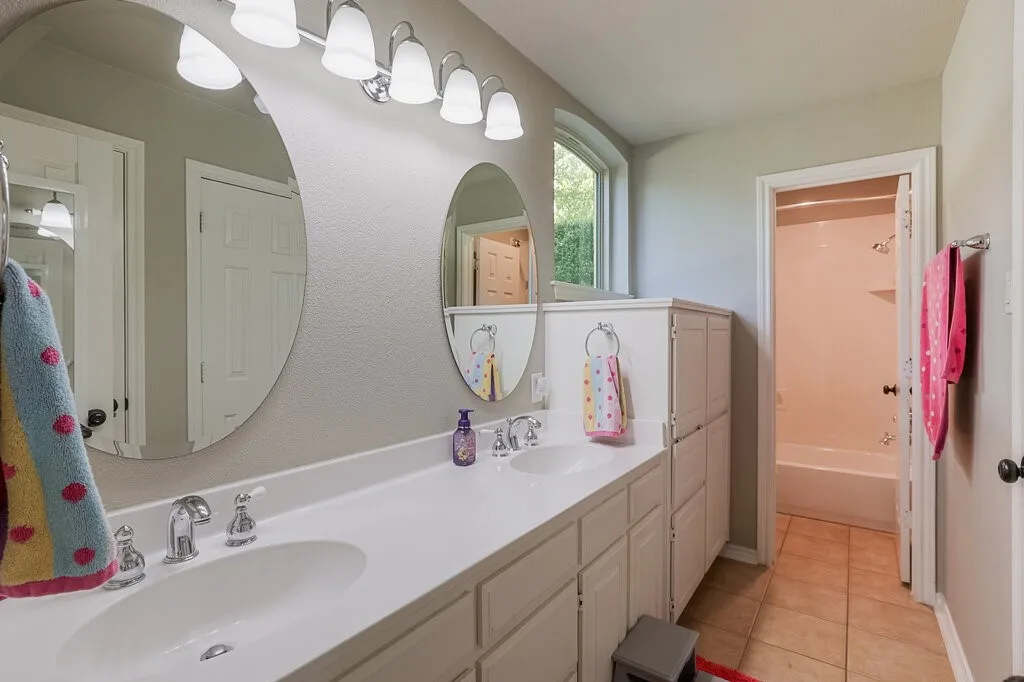 Double vanity featuring integrated sinks, white countertops, two oval wall-mounted mirrors, and an arched window