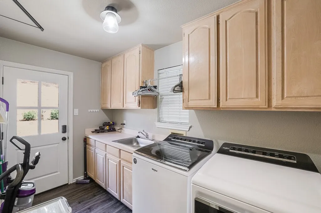 Laundry area featuring light wood cabinetry, integrated sink, solid-surface countertop, and exterior door with glass panes