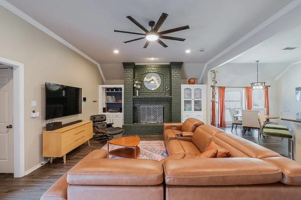 Living area featuring a floor-to-ceiling painted brick fireplace, built-in shelving, vaulted ceilings, multi-blade ceiling fan, and wood-finish flooring