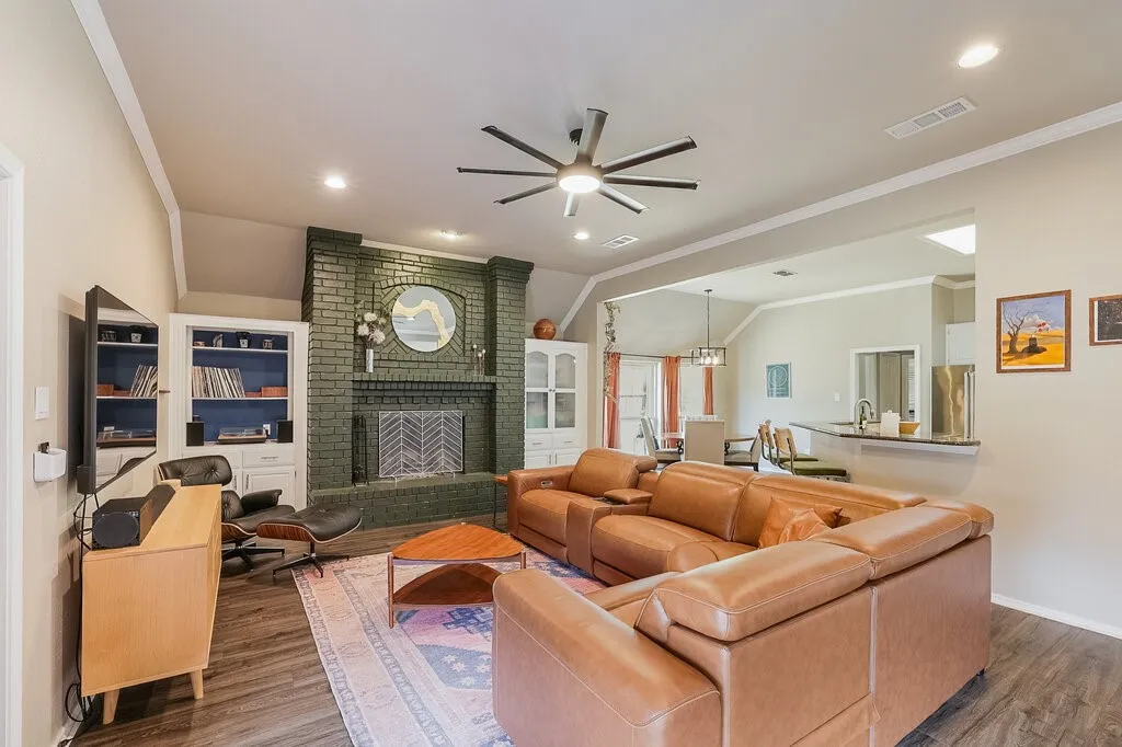 Vaulted ceilings, painted brick fireplace with integrated shelving, multi-blade ceiling fan, recessed lighting, and wood-finish flooring