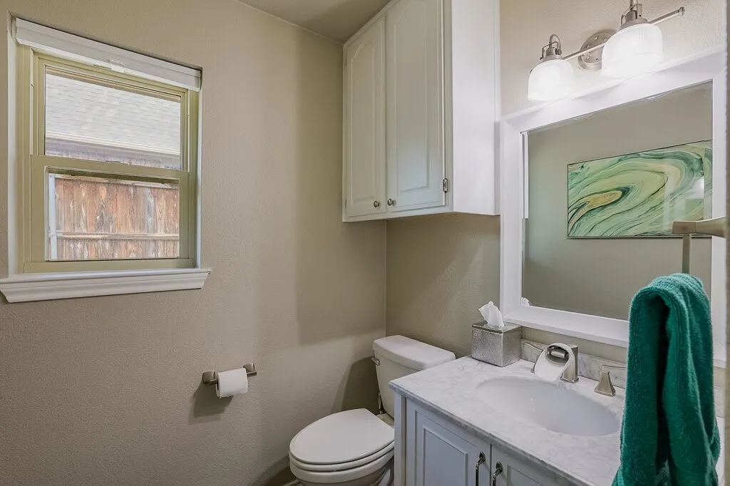 1/2 Bathroom featuring white shaker-style cabinetry, stone-finish vanity countertop, integrated sink, wall-mounted upper storage, and dual-bulb vanity lighting