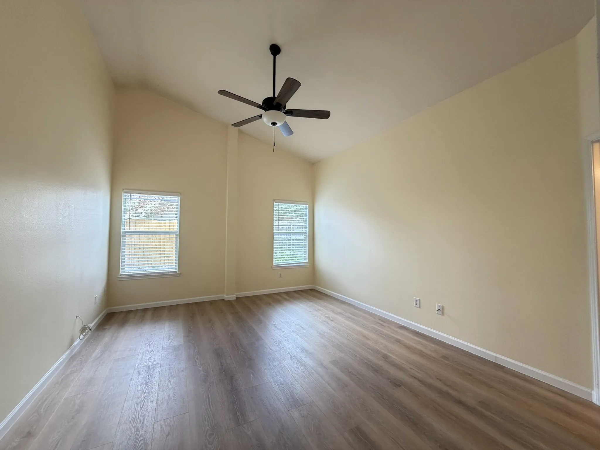 Vaulted ceilings featuring a multi-blade ceiling fan, wood-finish flooring, and dual windows with blinds