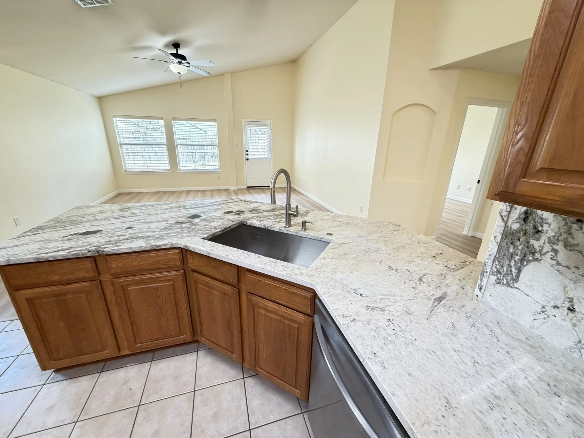Kitchen featuring natural stone countertops, under-mount stainless steel sink, gooseneck faucet, wooden cabinetry, and tiled flooring