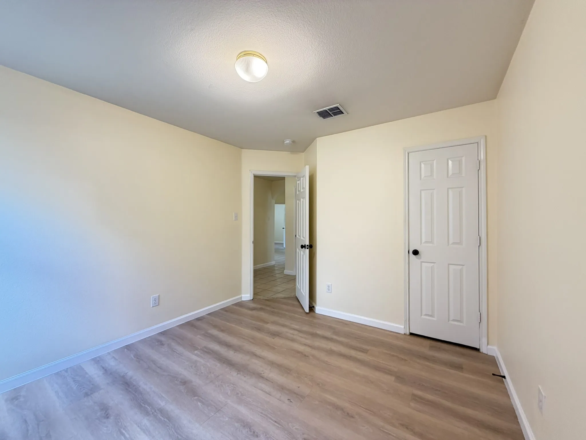 Room featuring wood-finish flooring, neutral wall paint, and a six-panel door with matte black hardware