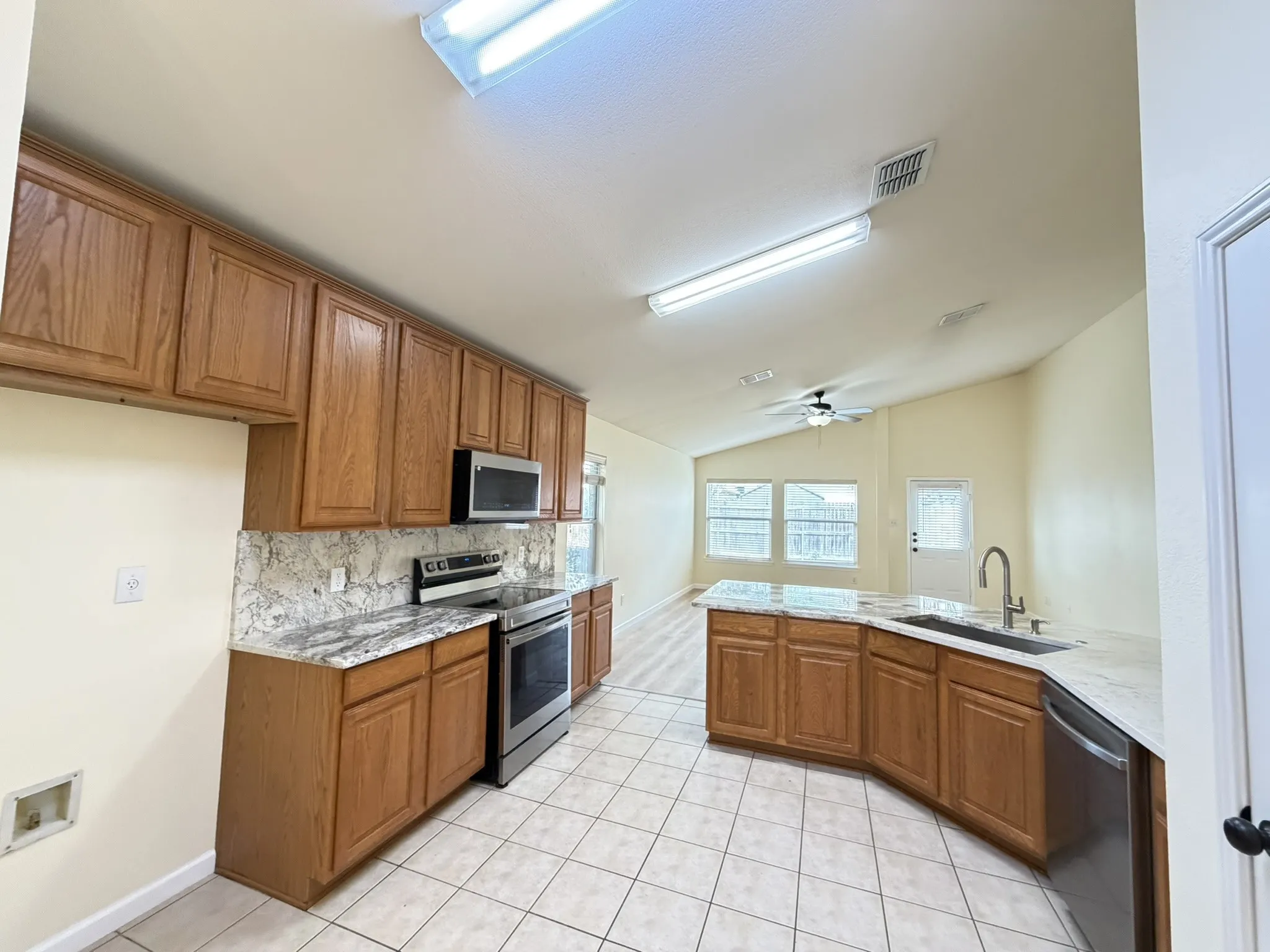 Kitchen featuring wood cabinetry, stone-patterned countertops, stainless steel appliances, and ceramic tile flooring