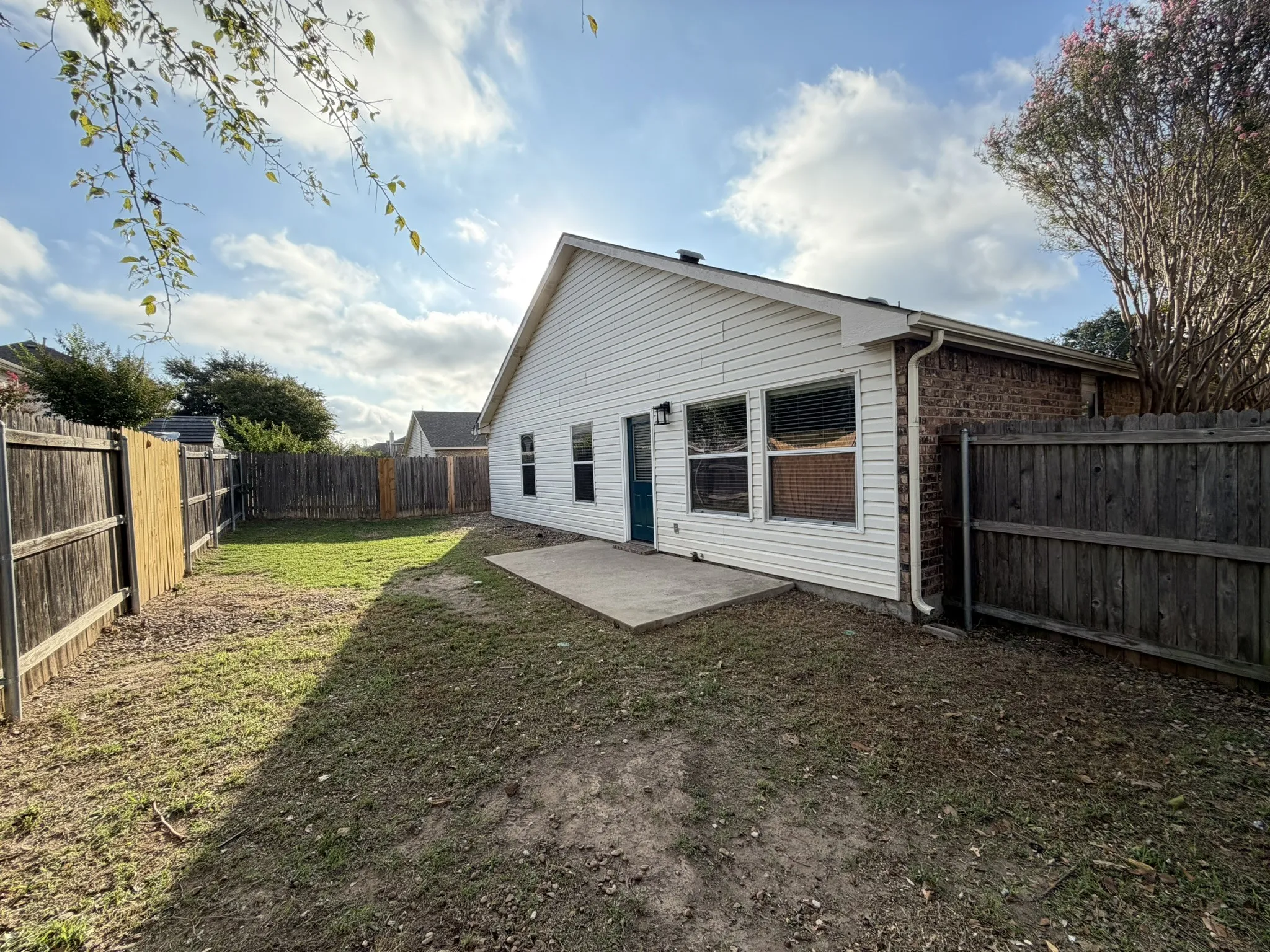 Rear exterior featuring horizontal vinyl siding, a brick facade section, a concrete patio, and a wood privacy fence
