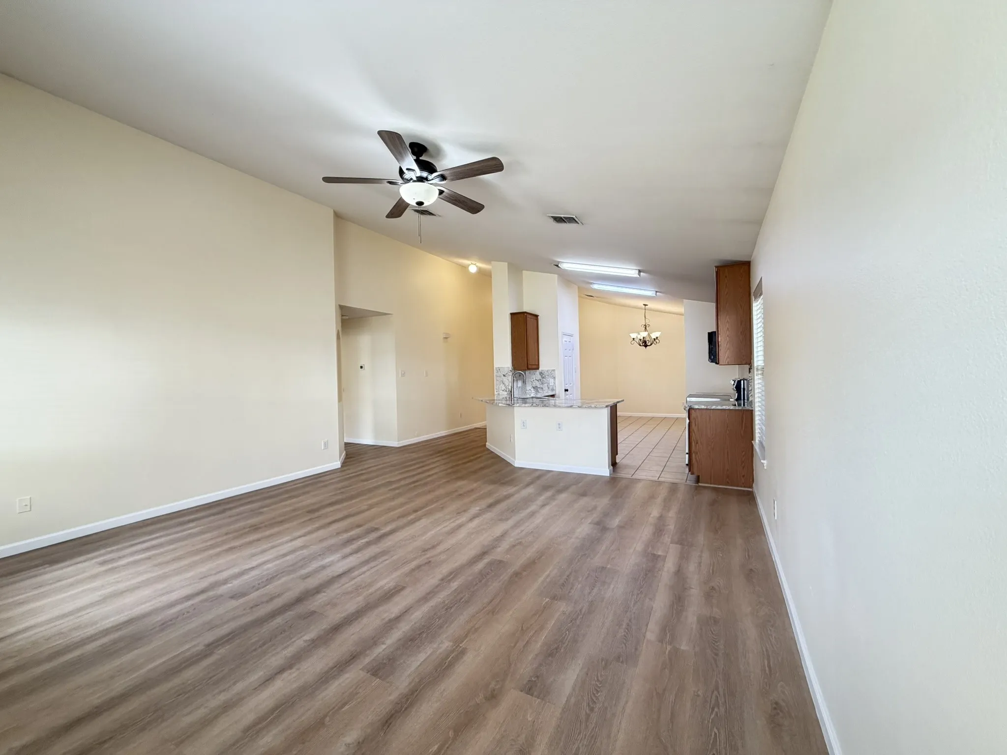 Open-concept interior featuring vaulted ceilings, wood-finish flooring, a kitchen peninsula with stone-finish countertops, and a ceiling-mounted light fixture