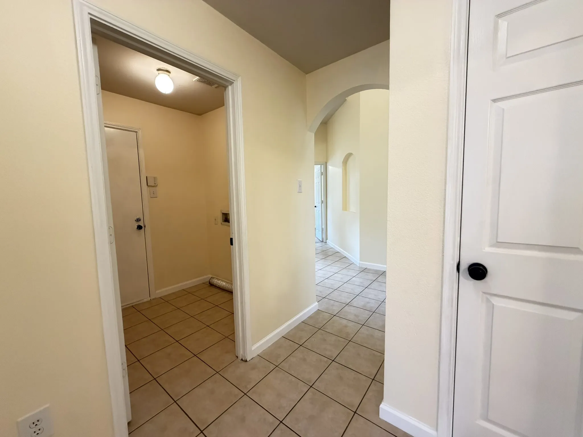 Interior hallway featuring neutral ceramic tile flooring, architectural archways, and a multi-panel door with matte black hardware