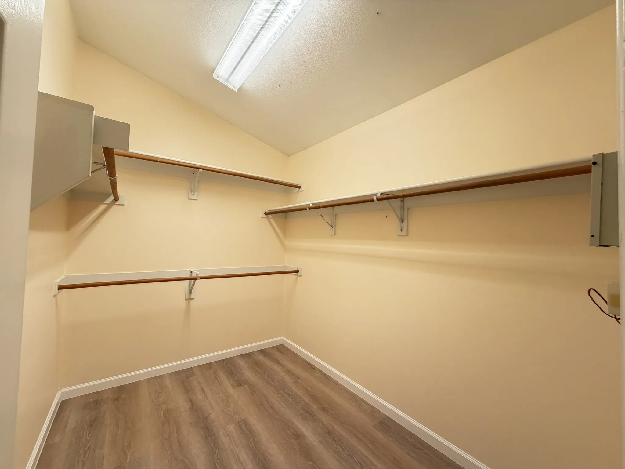 Walk-in storage space featuring wood-finish flooring, multi-level shelving with integrated hanging rods, and a vaulted ceiling with flush-mount lighting