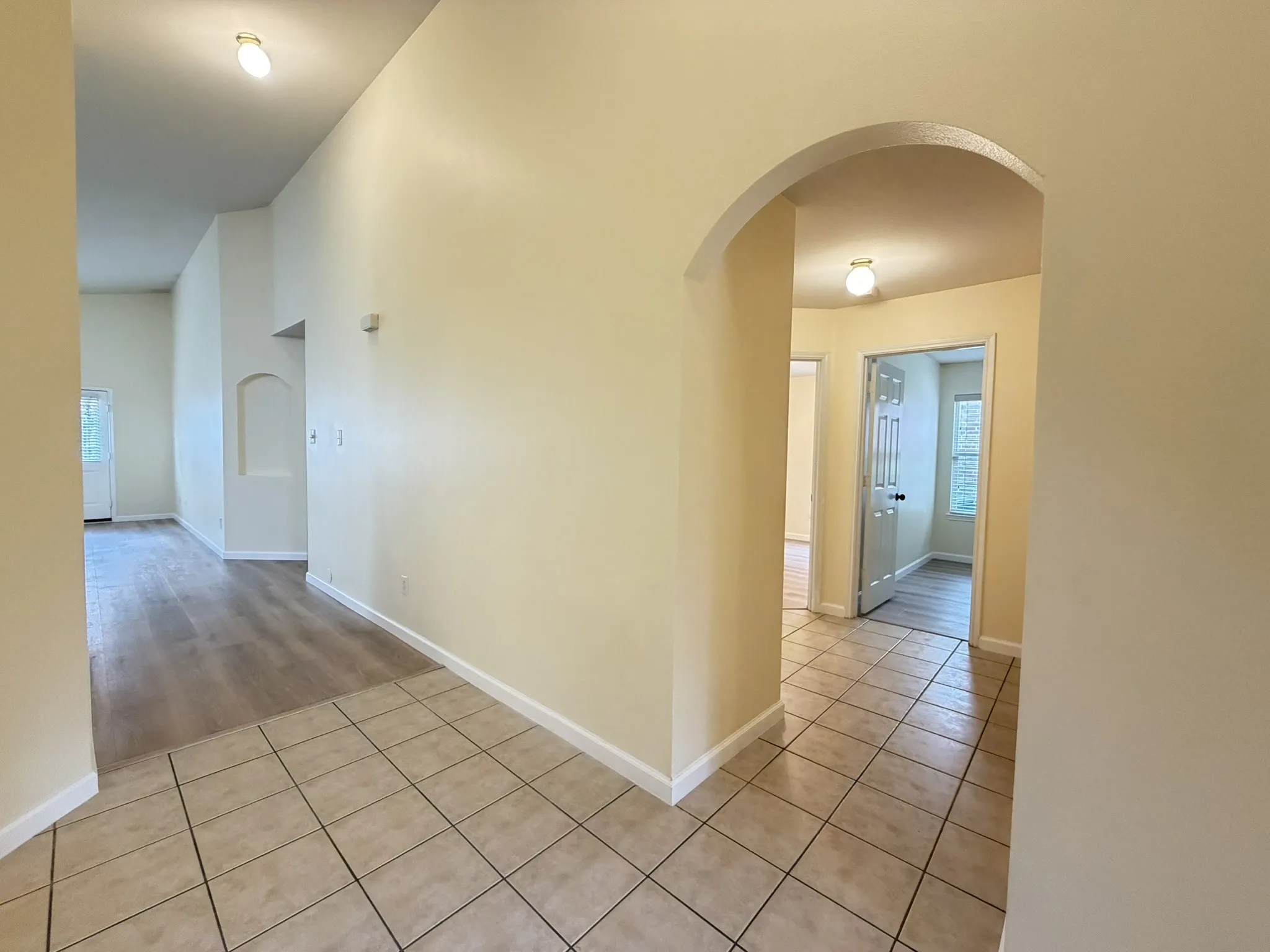 Interior featuring vaulted ceilings, arched passage, recessed wall niche, ceramic tile flooring, and wood-finish flooring