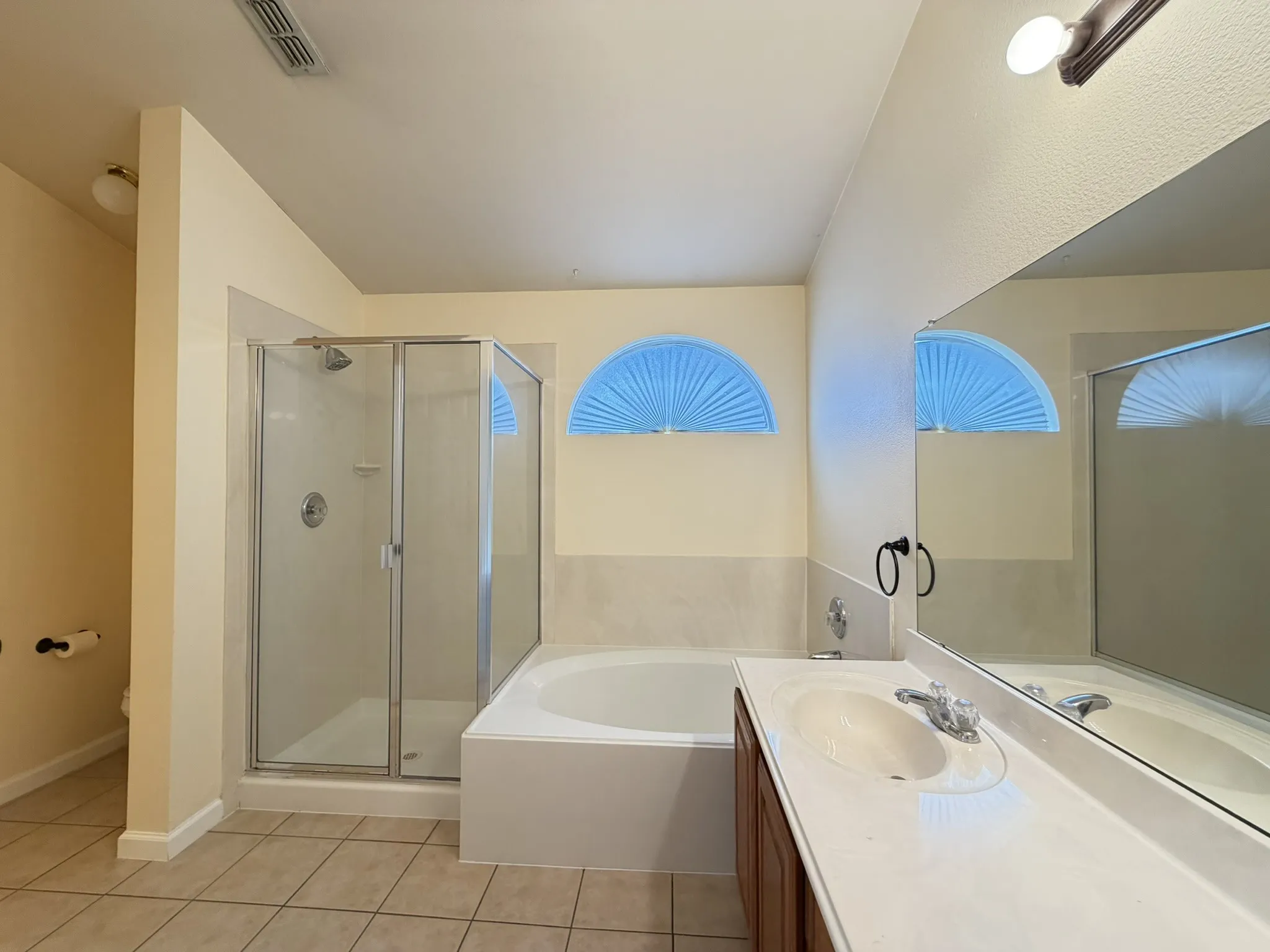 Bathroom featuring a glass-enclosed shower, soaking tub, vanity with light-toned countertop and integrated sink, large wall-mounted mirror, and tile flooring
