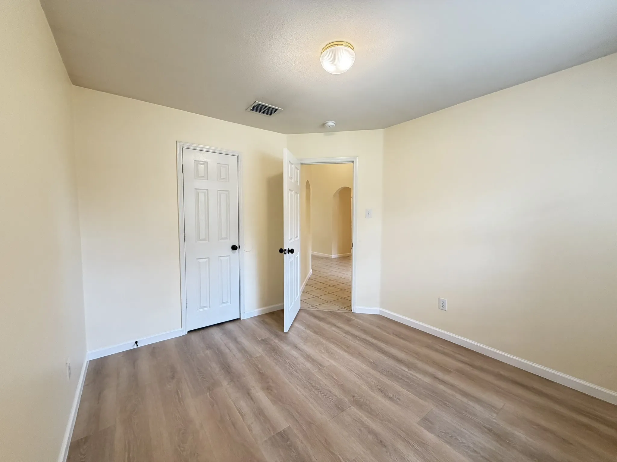 Interior space featuring wood-finish flooring, neutral wall tones, a six-panel door, and a flush-mount ceiling light