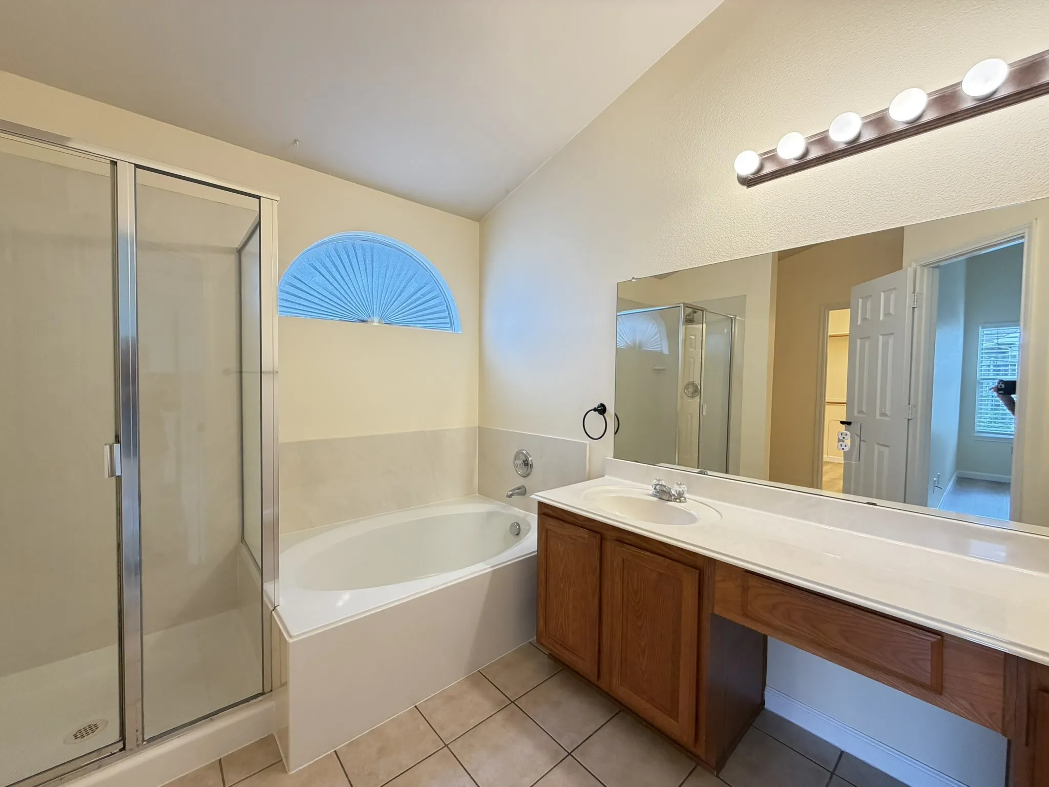 Bathroom featuring a glass-enclosed shower, deep soaking tub, arched transom window, wood-finish vanity with countertop, and large wall-mounted mirror