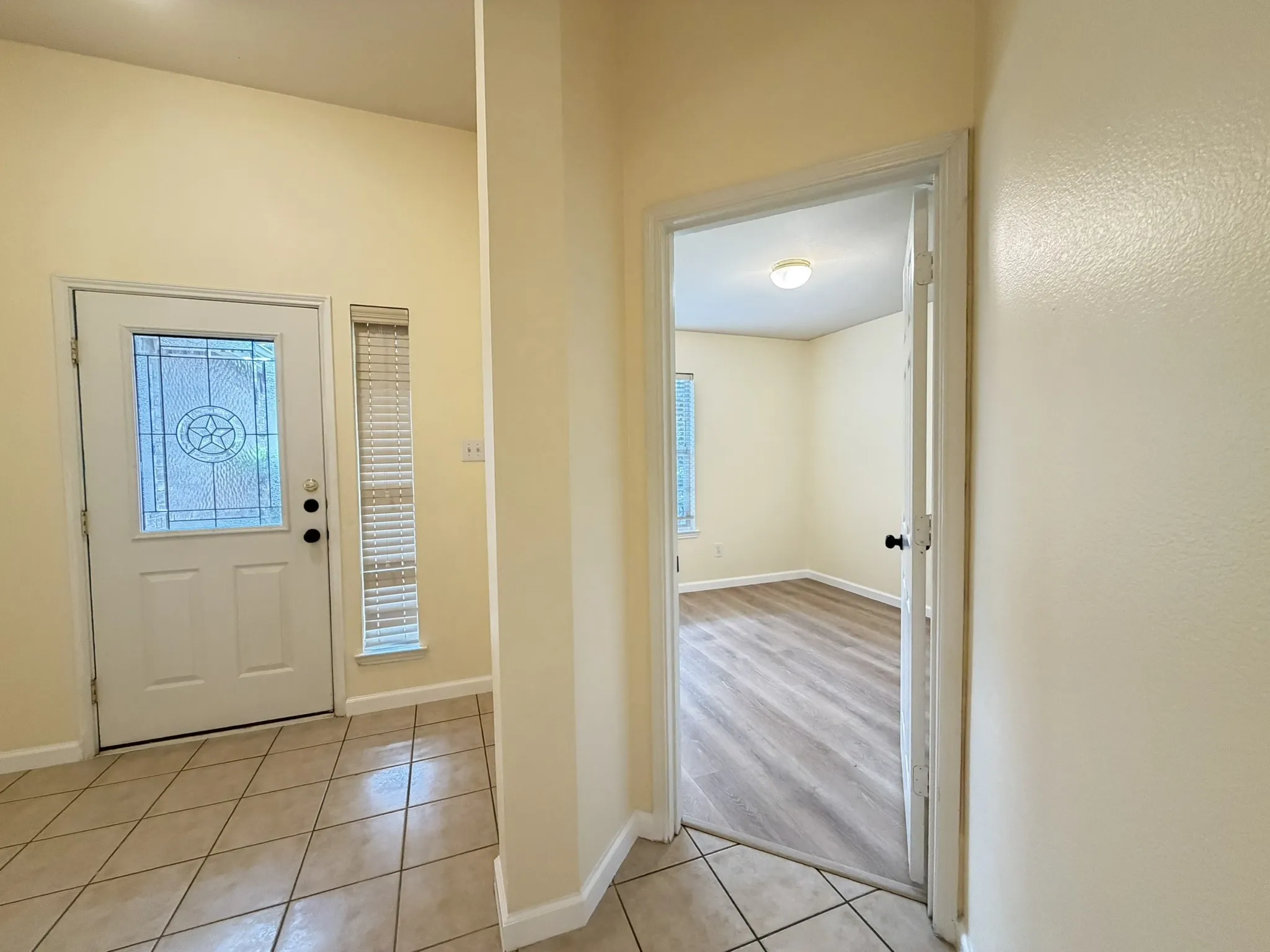 Entryway featuring a decorative glass-panel door, neutral tile flooring, and wood-finish flooring in the additional room