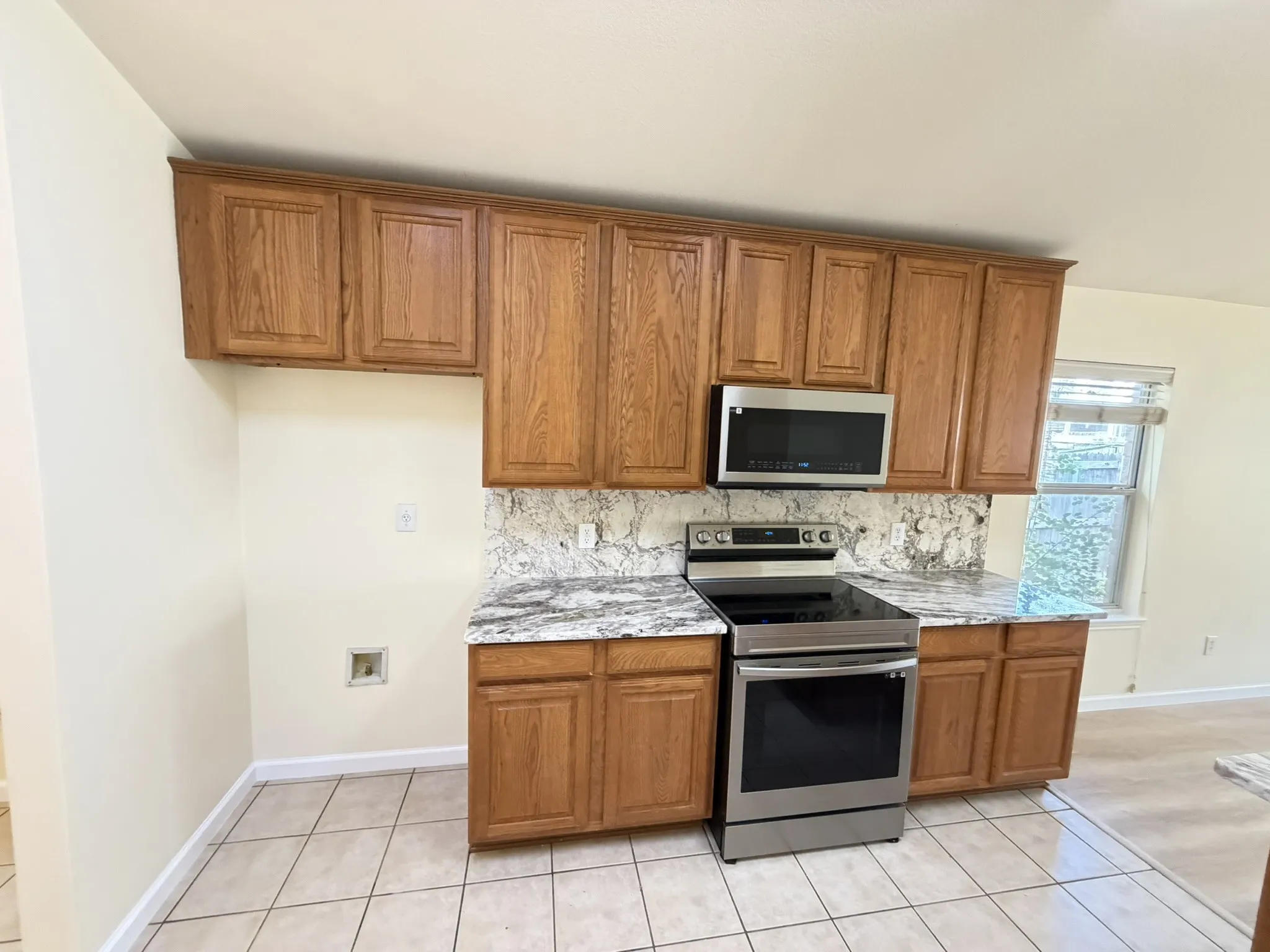 Natural wood-finish cabinetry, patterned stone-finish countertops, stainless steel electric range, over-the-range microwave, and ceramic tile flooring