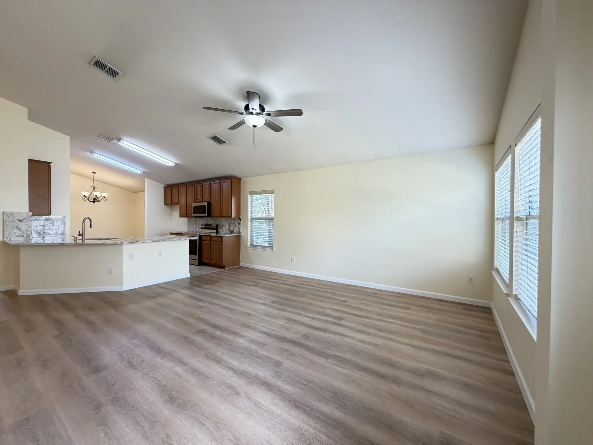 Open-concept interior featuring wood-finish flooring, vaulted ceilings, a kitchen peninsula with stone-finish countertops, built-in cabinetry, and integrated ceiling fans