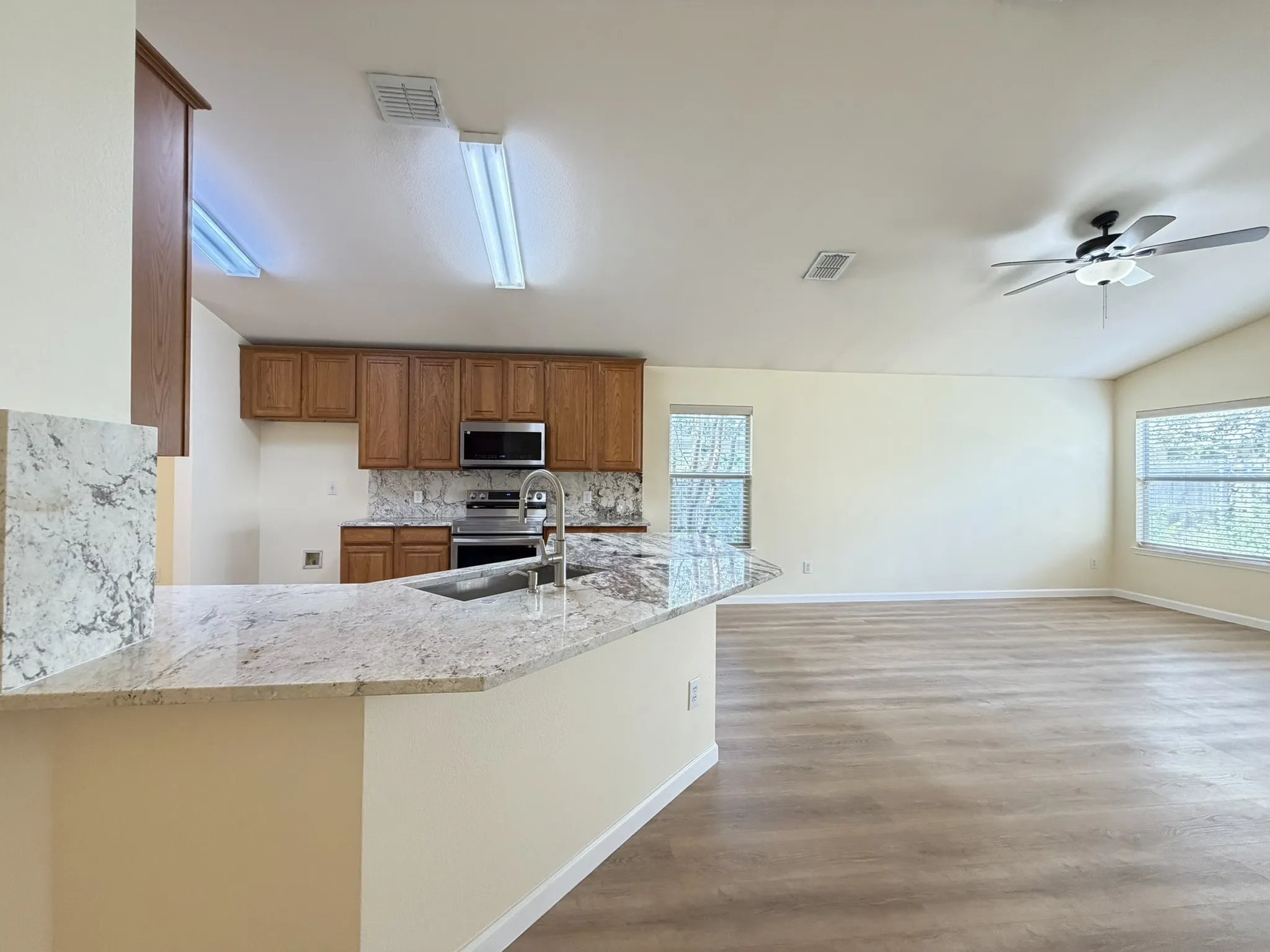 Kitchen featuring wood cabinetry, stone-surface countertops, stainless steel appliances, wood-finish flooring, and vaulted ceilings