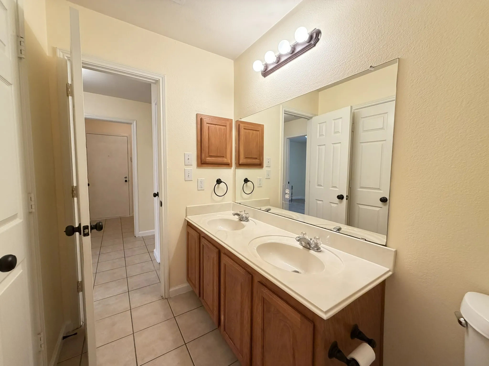 Double vanity featuring wood-finish cabinetry, integrated dual sinks, a large wall-mounted mirror, and a four-bulb vanity light fixture