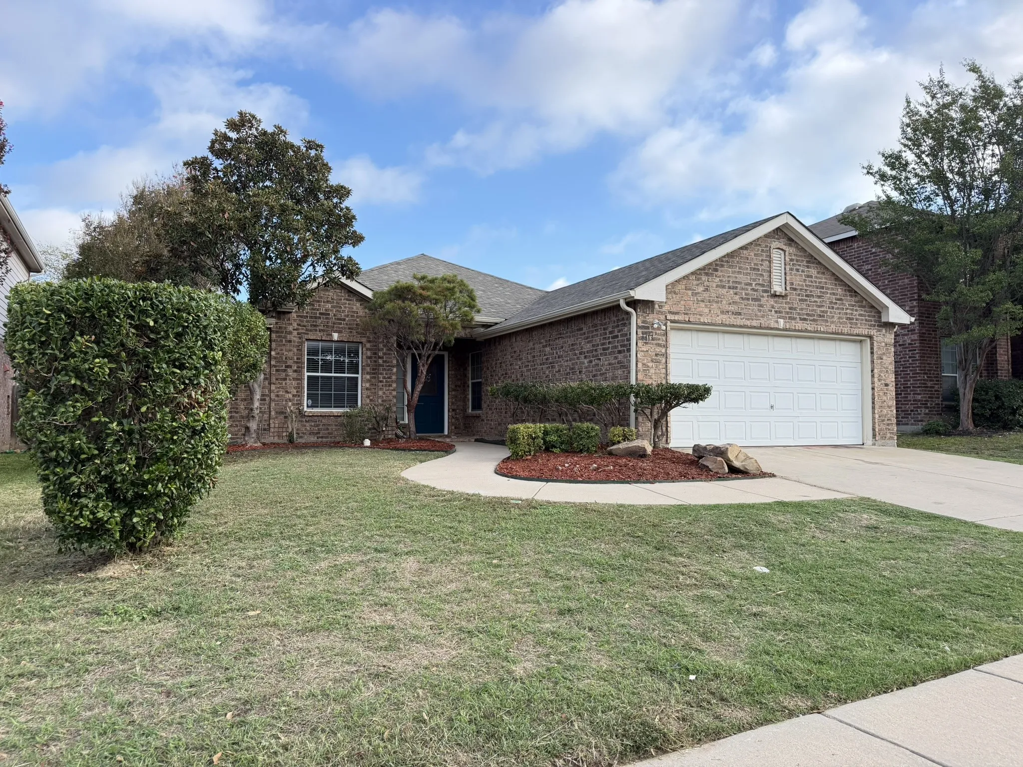 Brick exterior featuring a gabled roofline, a two-car garage with a panel door, and a curved concrete walkway