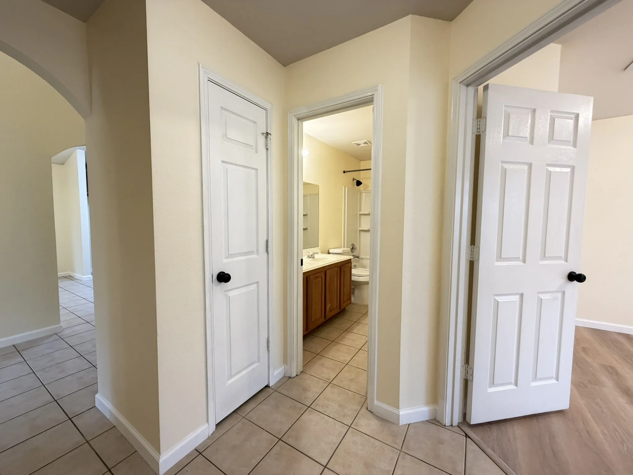 Neutral-toned interior featuring ceramic tile flooring, six-panel interior doors with matte black hardware, and an accessible bathroom containing a wood-finish vanity and integrated cabinetry