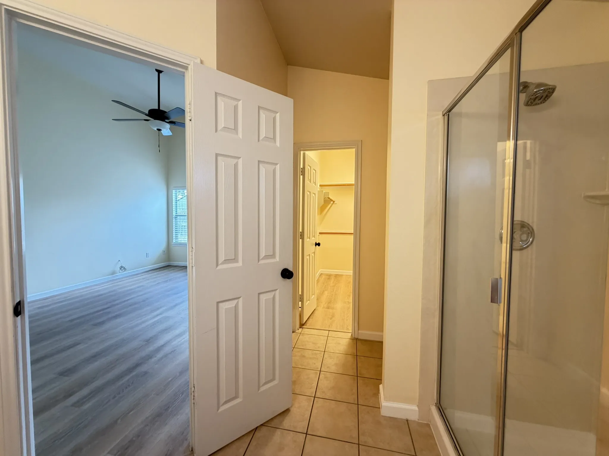 Shower with glass enclosure, ceramic tile flooring, wood-finish flooring, vaulted ceilings, and built-in closet shelving