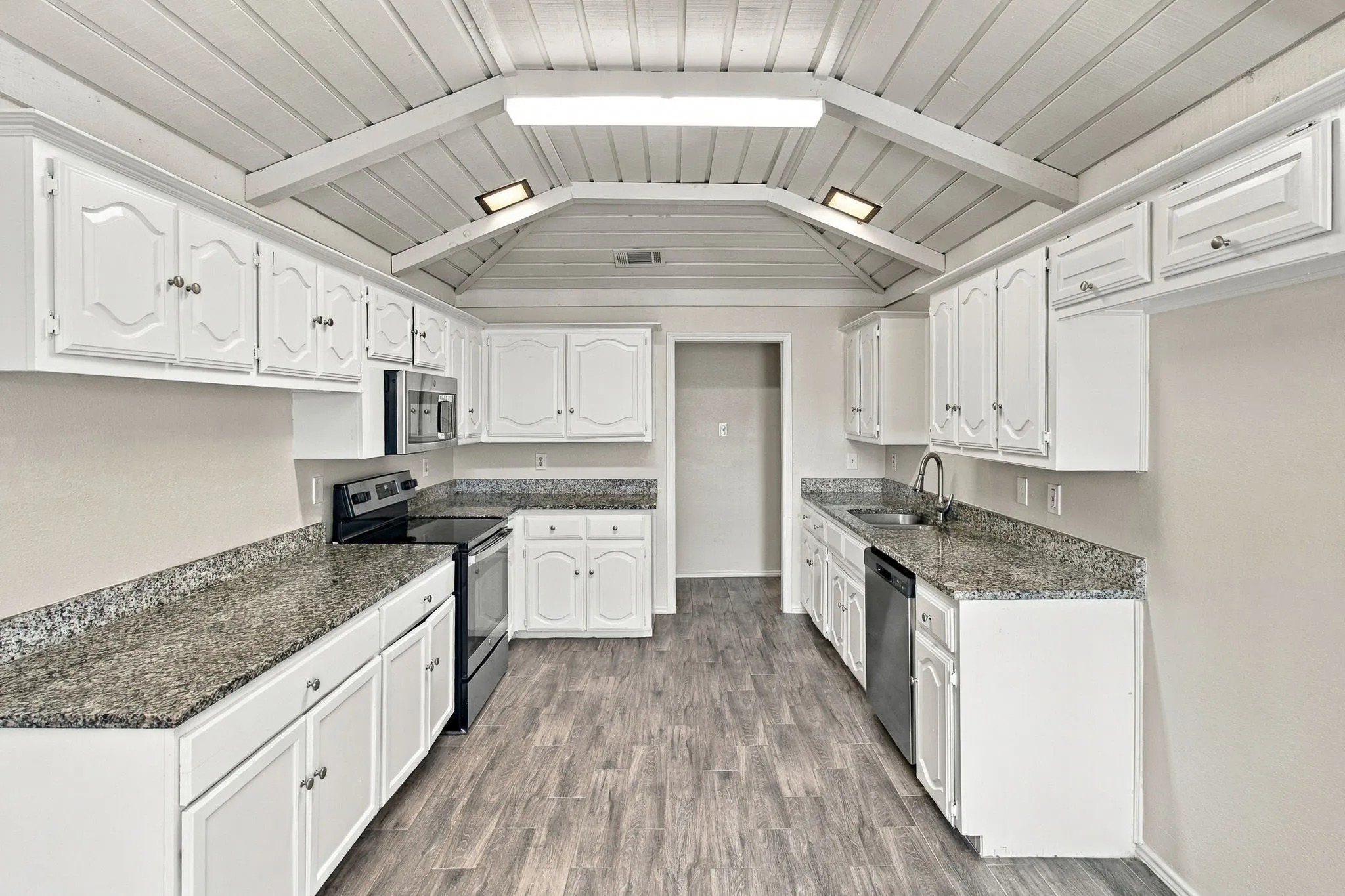 Kitchen featuring white cabinetry, stone-finish countertops, wood-finish flooring, vaulted ceilings with exposed beams, and stainless steel appliances
