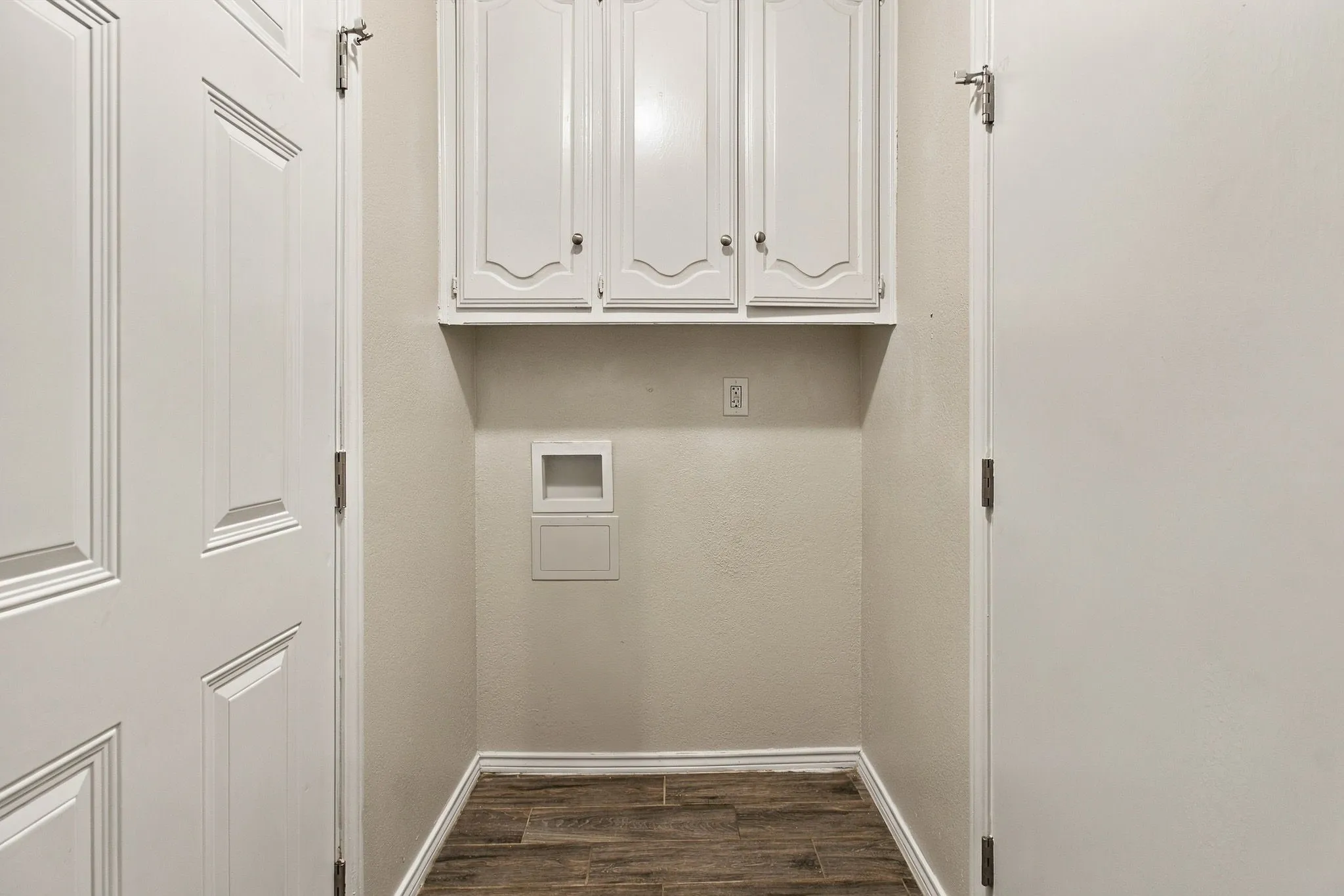 Utility area featuring upper wall-mounted cabinetry, wood-finish flooring, and recessed utility hookups