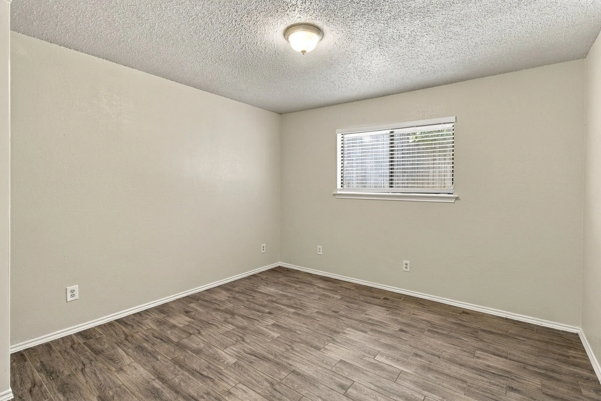 Interior room featuring wood-finish flooring, neutral wall paint, and a central flush-mount ceiling light fixture with an inset window