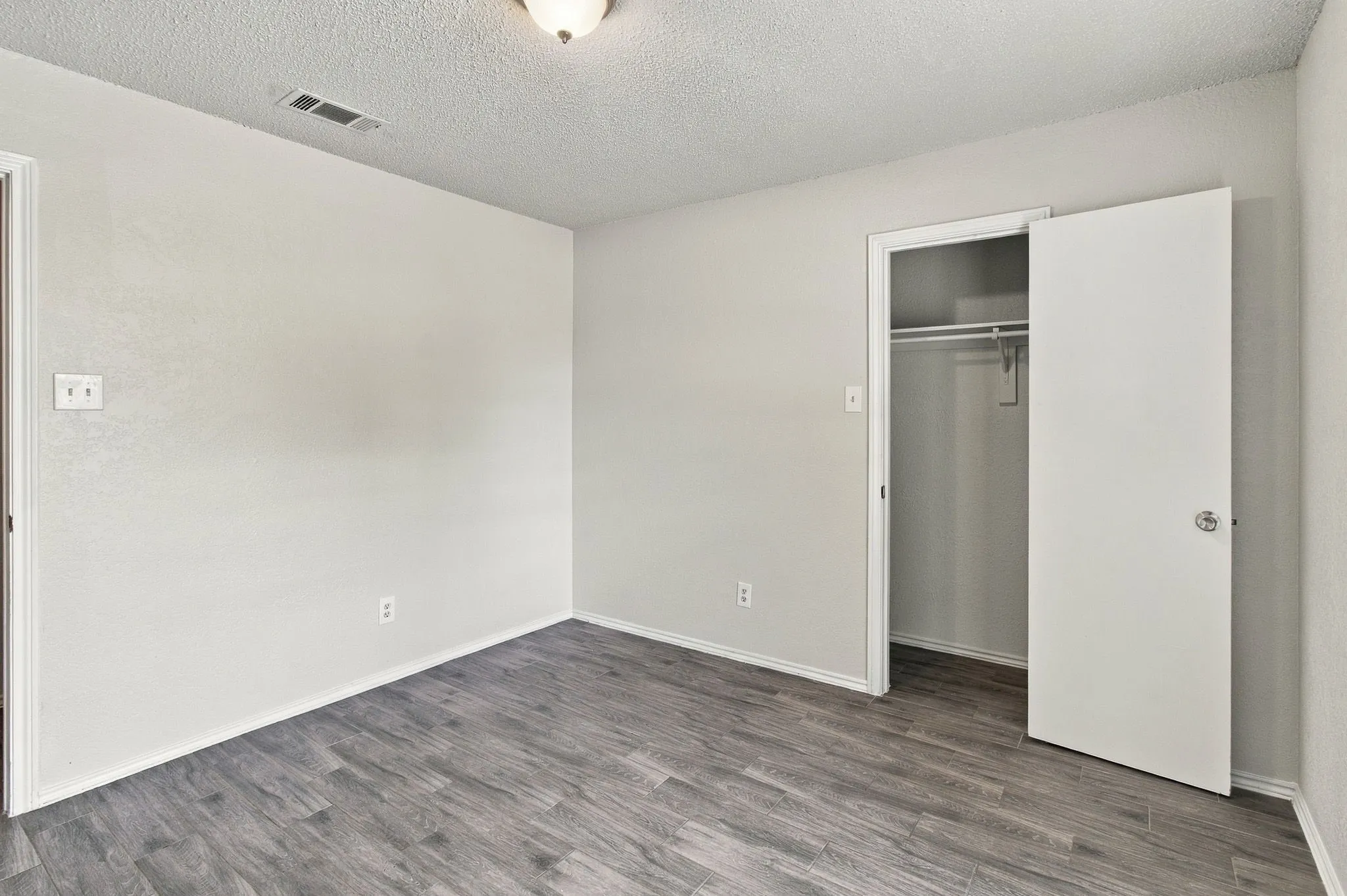 Interior room featuring wood-finish flooring, neutral wall paint, and a reach-in closet with an integrated rod