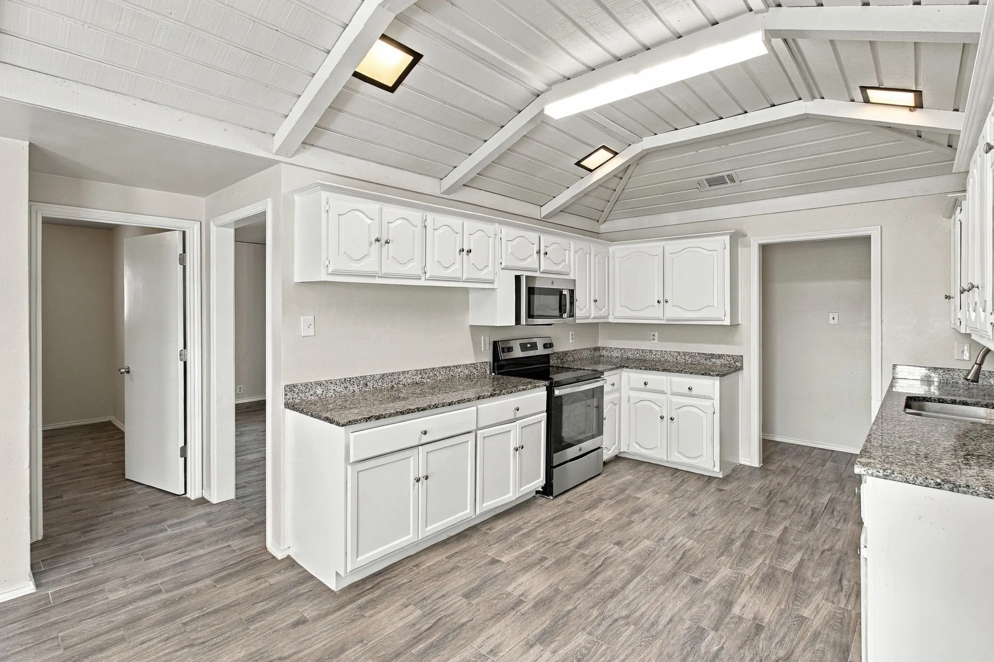 Kitchen featuring vaulted tongue-and-groove ceilings, white cabinetry, stone-finish countertops, stainless steel appliances, and wood-finish flooring