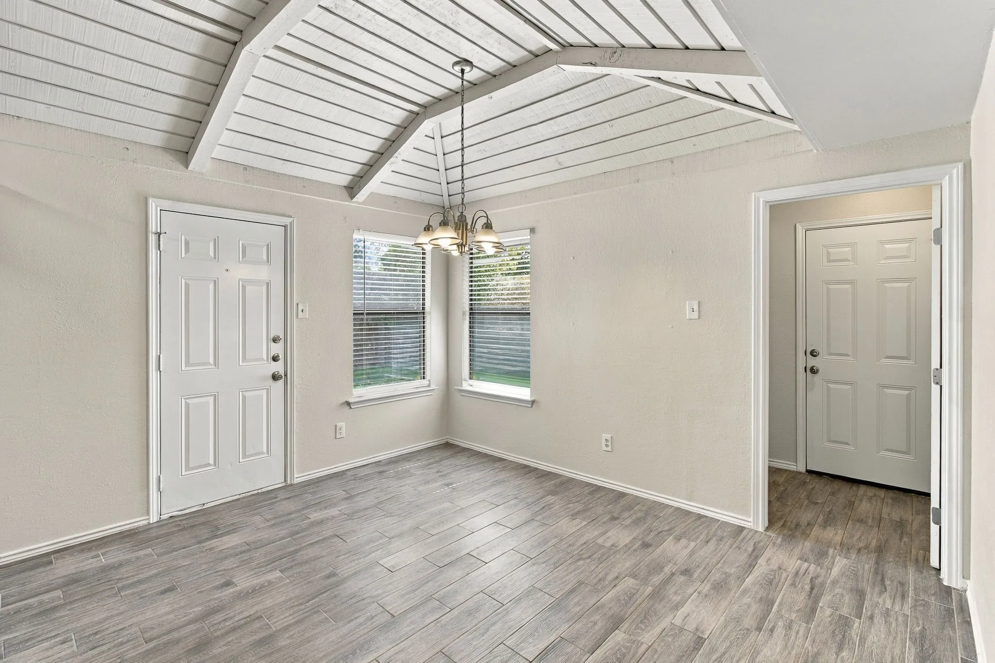 Vaulted ceiling with exposed wood-finish beams, wood-finish flooring, and a multi-arm pendant light fixture
