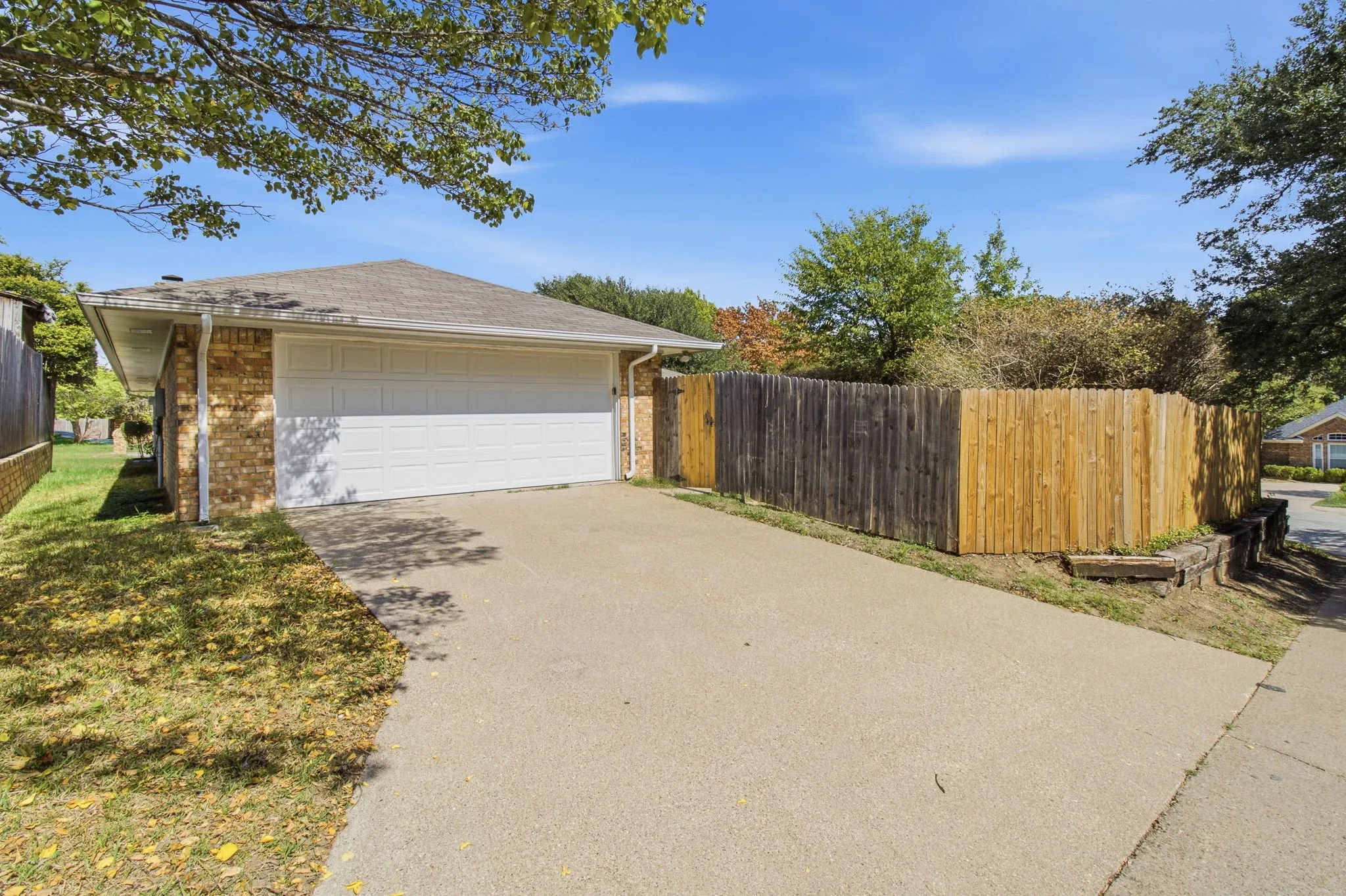 Attached two-car garage with white sectional door, concrete driveway, and wood privacy fencing