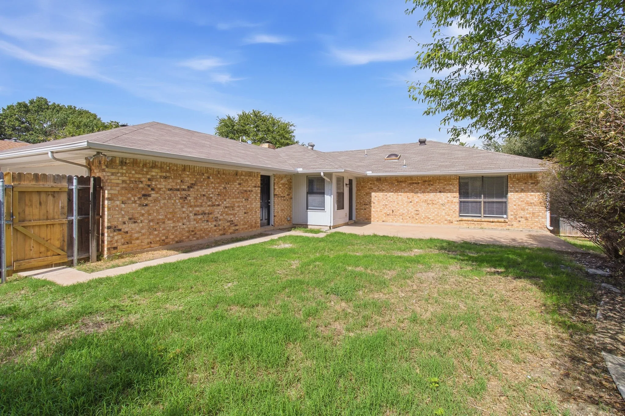 Rear exterior featuring a brick facade, concrete patio, wood privacy fencing, and a grass lawn