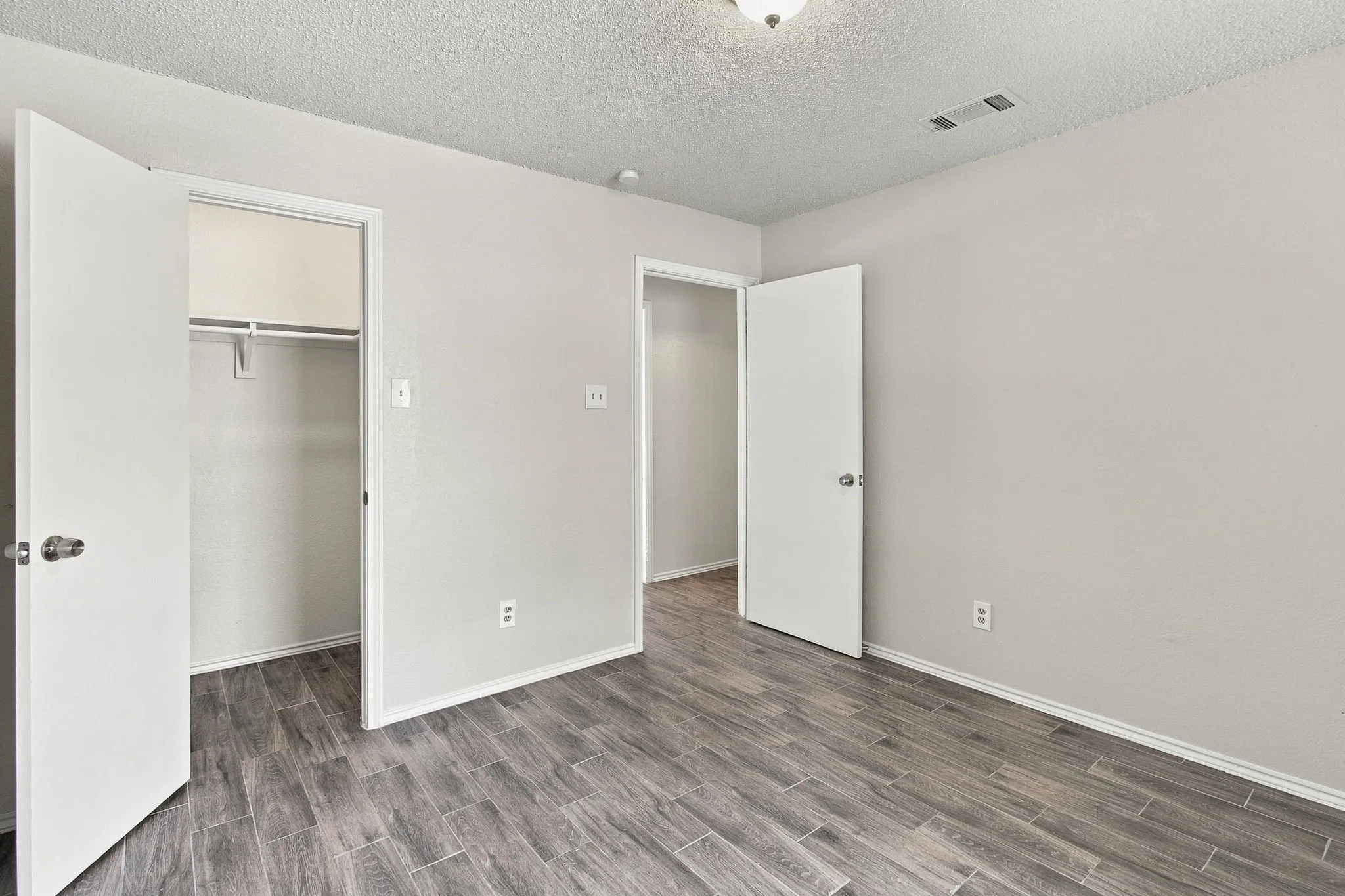 Room featuring neutral wall paint, wood-finish flooring, two interior doors, and a built-in closet with integrated shelving