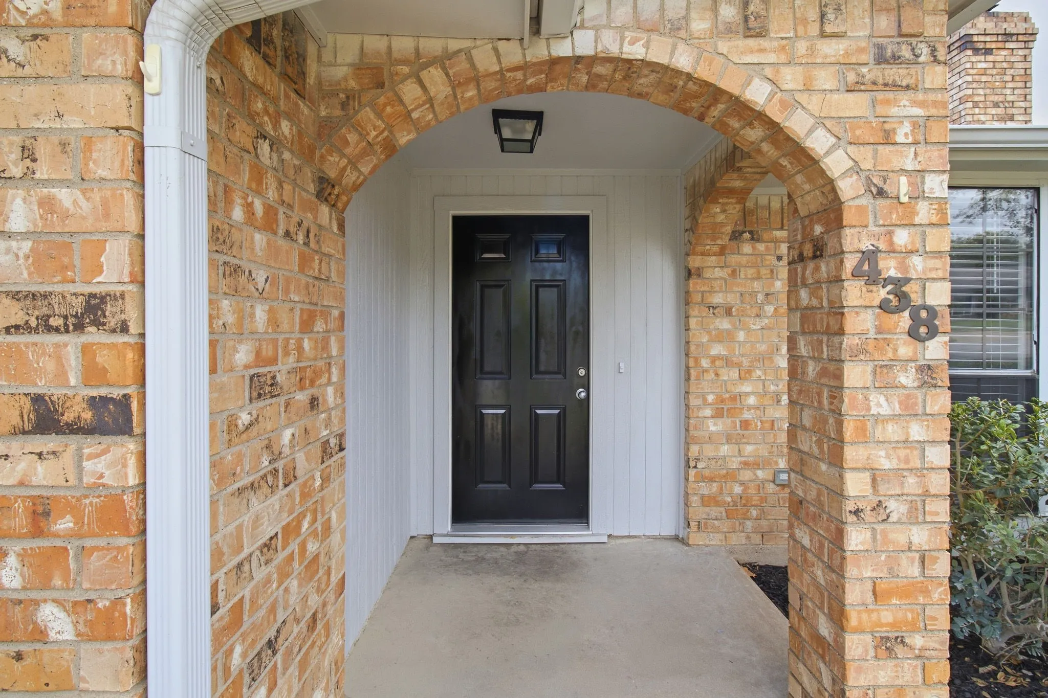 Covered entryway featuring a brick facade, arched masonry detailing, a solid-panel door, and an overhead flush-mount light fixture