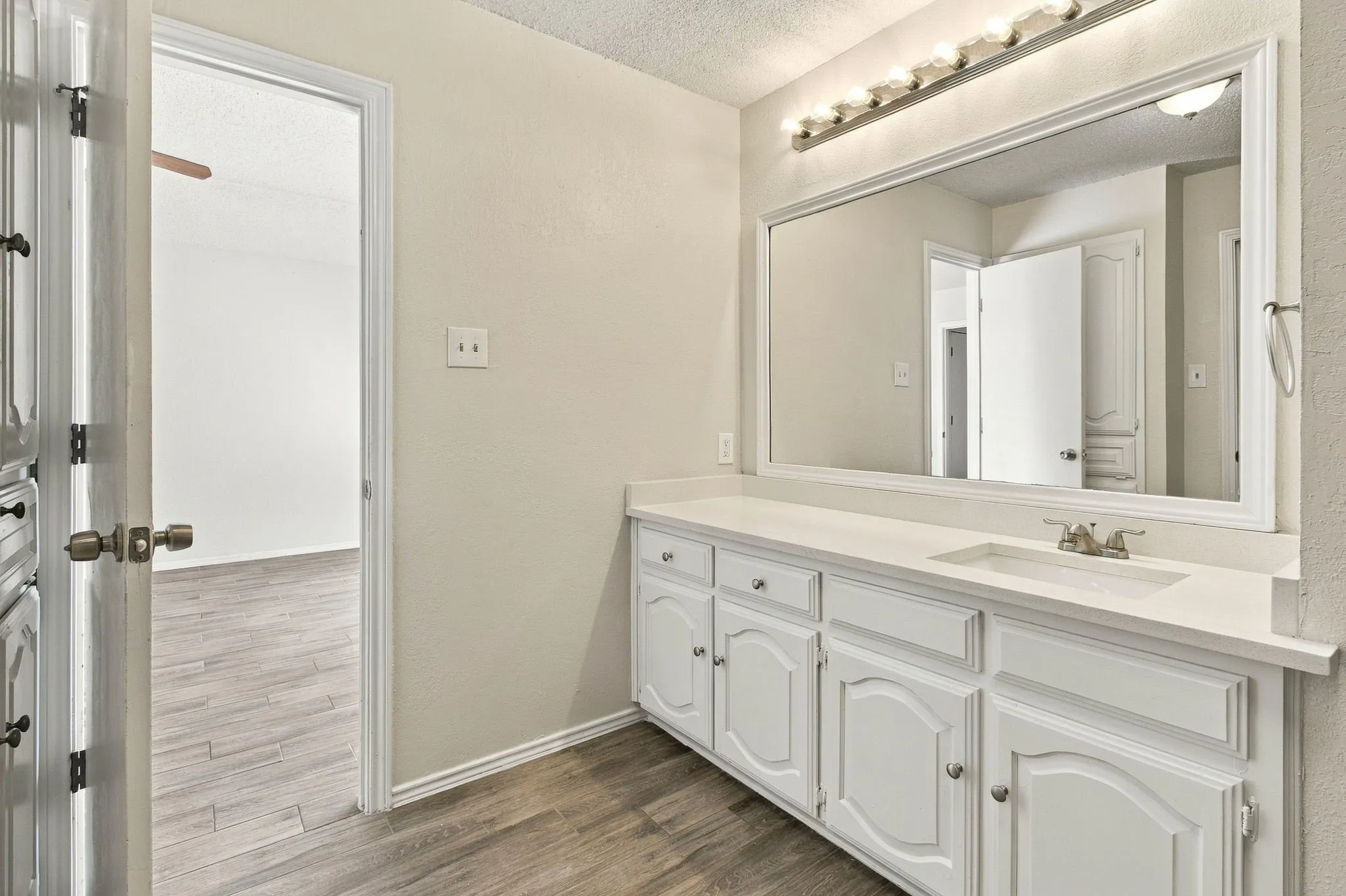 Vanity featuring white built-in cabinetry, a wide countertop, a large framed mirror, and a multi-bulb light fixture