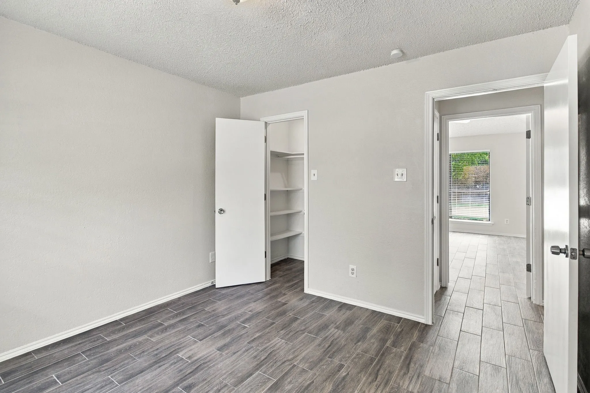 Interior room featuring wood-finish tile flooring, neutral wall paint, and a built-in closet with integrated shelving